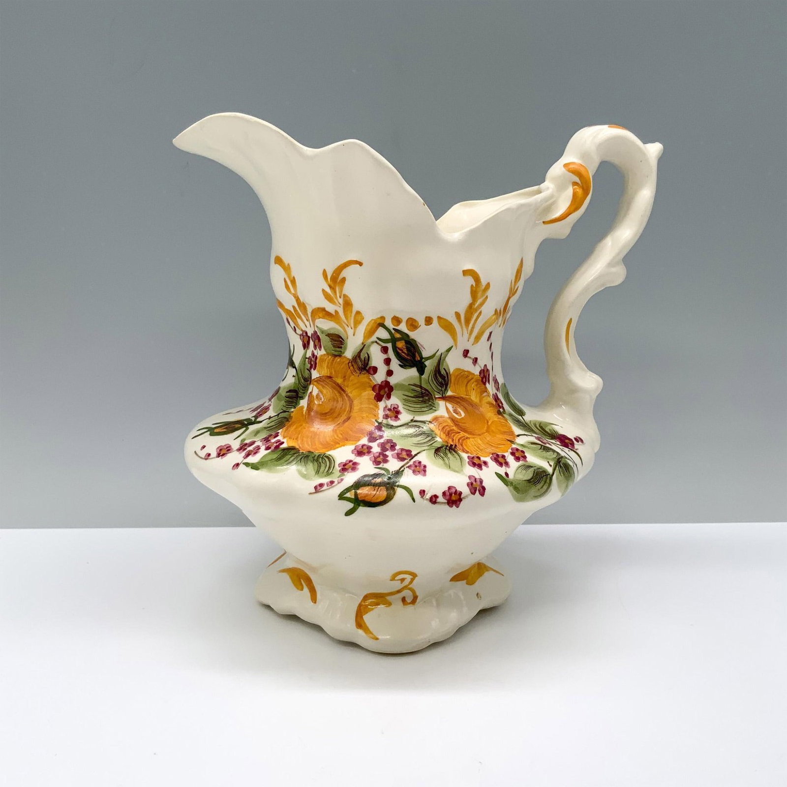 Cash Family Art Pottery Pitcher, Marigolds: A spacious white pitcher adorned with vibrant marigolds, red daisies, and lush foliage painted across its wide body. Cash Family backstamp. Dimensions: 6"L x 5.5"W x 6.5"H Manufacturer: Cash Family Co