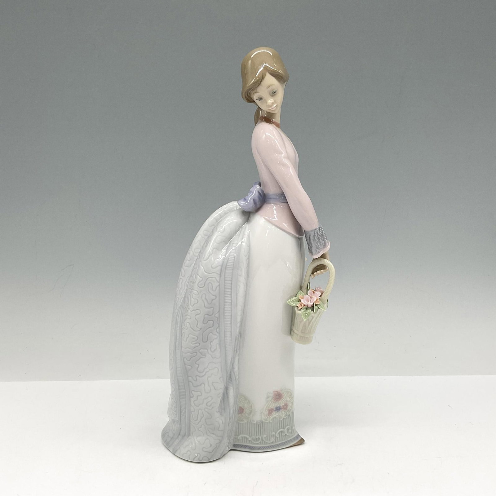 Basket Of Love 1007622 - Lladro Porcelain Figurine: Glossy Collectors Society figure of young girl with basket of flowers. Lladro backstamp. Artist: Jose Puche Issued: 1994 Dimensions: 3.5"L x 3.5"W x 9.75"H Manufacturer: Lladro Country of Origin: