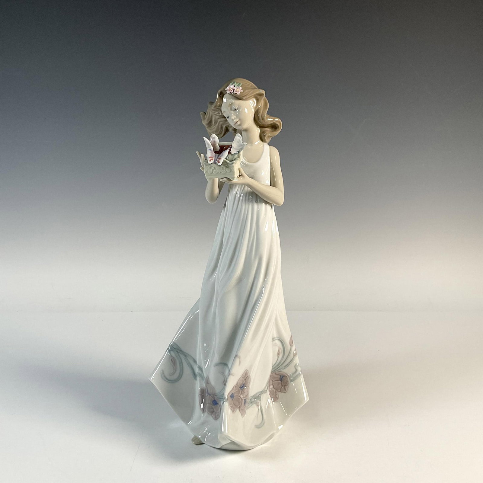 Butterfly Treasures 1006777 - Lladro Porcelain Figurine: Glossy figure holding a basket with butterflies around it. Lladro backstamp. This item has its original box: 8.5"L x 15"W x 7"H. Artist: Marco Antonio Nogueron Issued: 2001 Dimensions: 6"L x 6"W x 12.