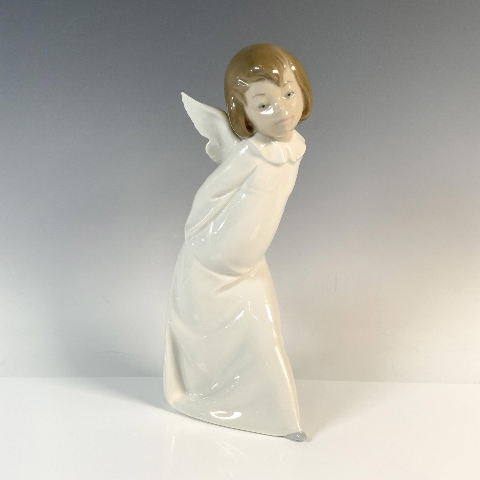 Cherub Smiling 1004960 - Lladro Porcelain Figurine: Angel Farolero with glossy finish and Lladro backstamp. This angel with small wings on her back and a full-length white dress is bent over to look at something. Lladro backstamp. Artist: Salvador Debo