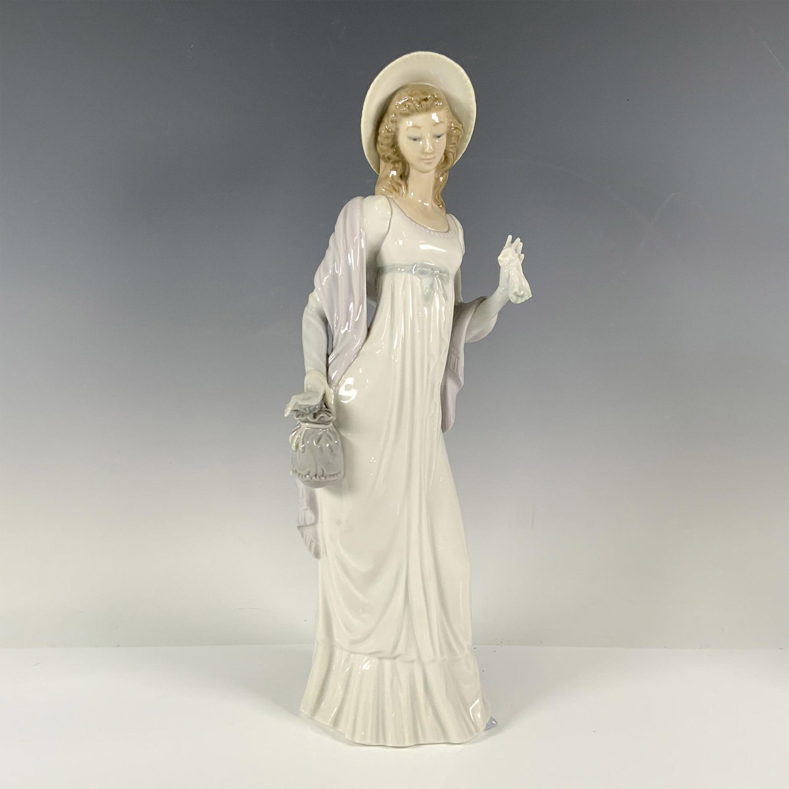 Dainty Lady 1004934 - Lladro Porcelain Figurine: Glossy finish, features an elegant lady, dressed in white clothes with blue details. Lladro backstamp. Artist: Vicente Martinez Issued: 1974 - 1985 Dimensions: 4''L x 6''W x 14''H Manufacturer: Lladro