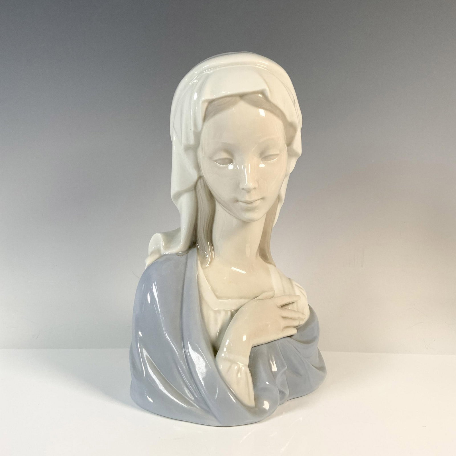 Madonna Head 1004649 - Lladro Porcelain Bust: Glossy figure of the Virgin Mary wrapped in a blue shawl. Lladro backstamp. Artist: Vincente Martinez Issued: 1969-2001 Dimensions: 5.5"L x 4.5"W x 8.75"H Manufacturer: Lladro Country of Origin: