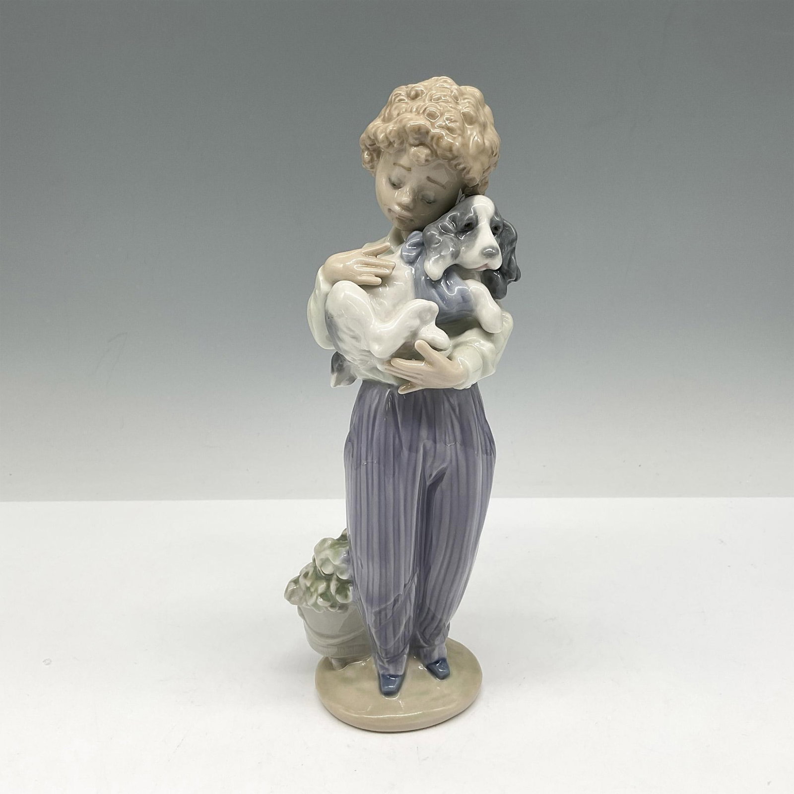 My Buddy 01007609 - Lladro Porcelain Figurine: Glossy figural holding his dog was Collectors Society figurine for 1989. Soft coloration of white, violet and sage. Lladro backstamp. This item has its original box: 5.5"L x 11"W x 5"H. Artist: Antoni