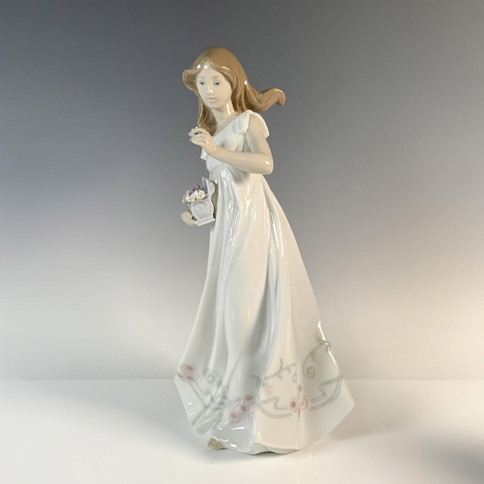 Treasures Of The Heart 1006554 - Lladro Porcelain Figurine: Glazed finish, lovely figure of a girl in a flowy white dress emborder with roses. She holds a box of delicate detailed flowers. Lladro backstamp. Includes the original box, dimensions: 7''L x 8.5''W 