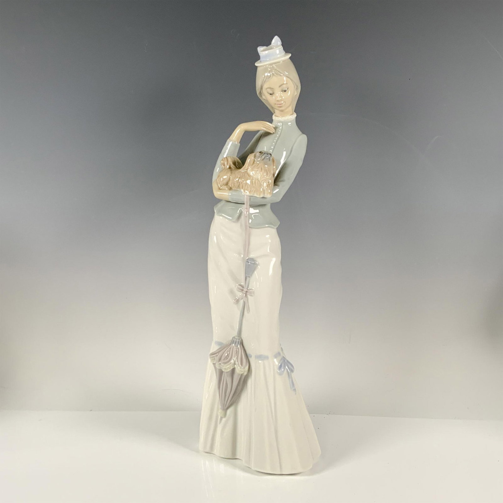 Walk with the Dog 1004893 - Lladro Porcelain Figurine: Glossy finish, features an elegant lady on a walk carrying her small dog. Lladro backstamp. Artist: Jorge Roig Issued: 1974 - 2004 Dimensions: 4.5''L x 4.5''W x 15''H Manufacturer: Lladro Country of