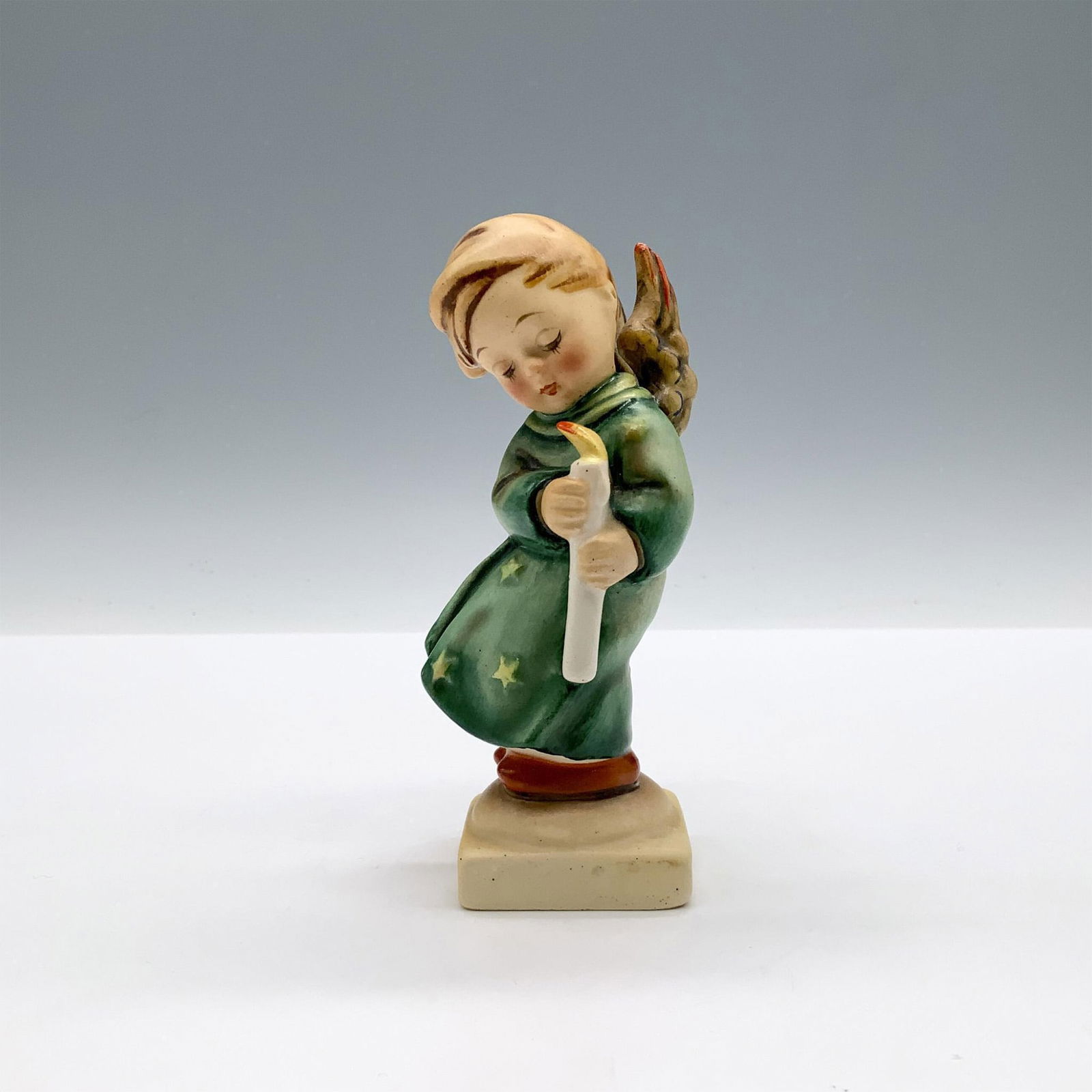 Goebel Hummel Porcelain Figurine, Heavenly Angel HUM21/0: A matte hand painted figure of an angelic child wearing a robe decorated with stars while holding a lit candle. Goebel backstamp. M.I. Hummel impressed. Issued: 1935-2010 Dimensions: 2"L x 1.5"W x 4.5