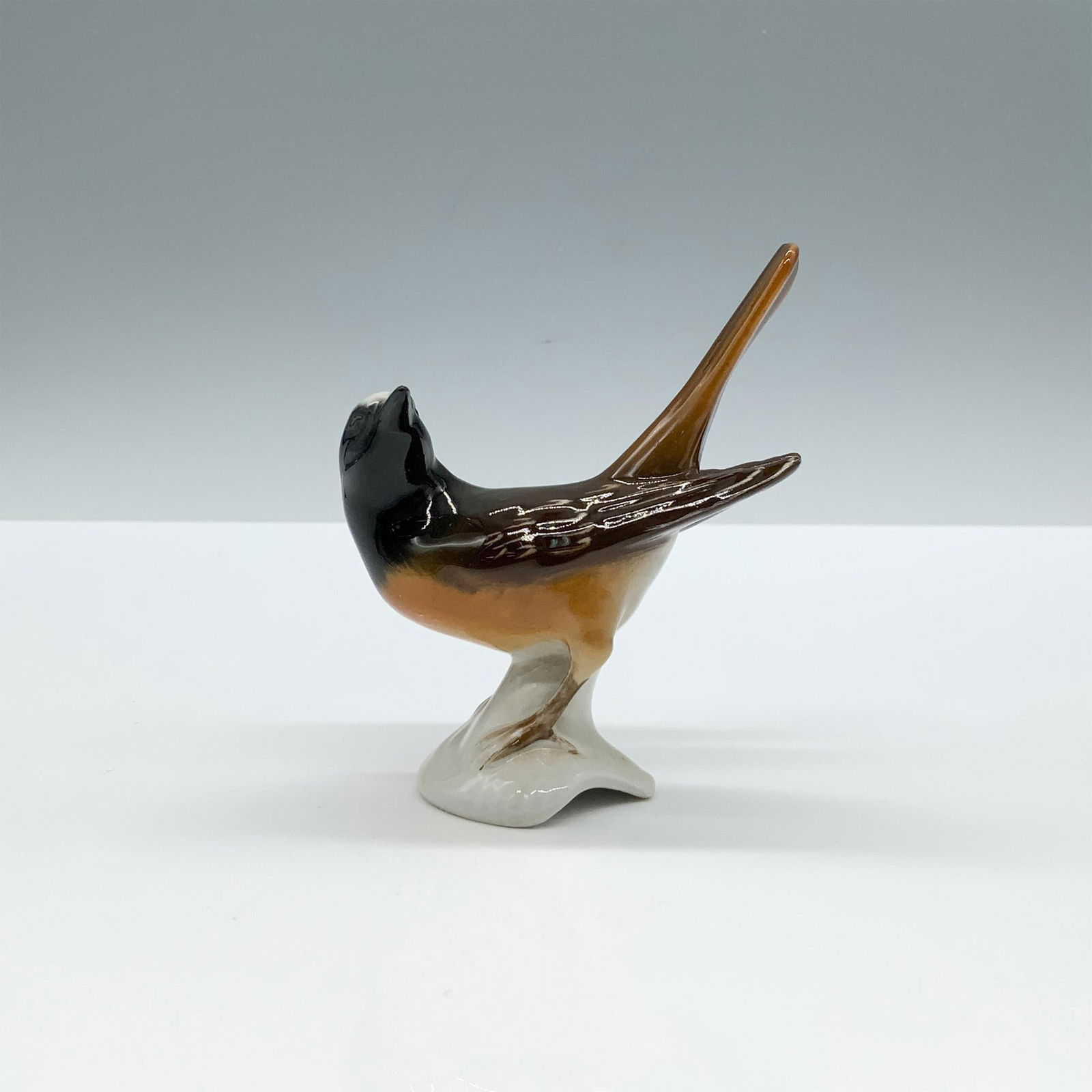 Goebel Bird Figurine, Redstart: A glossy sculpture of an alert bird with black, brown, and gray coloration. Goebel backstamp. Dimensions: 3.25"L x 1.75"W x 4"H Manufacturer: Goebel Country of Origin: Germany