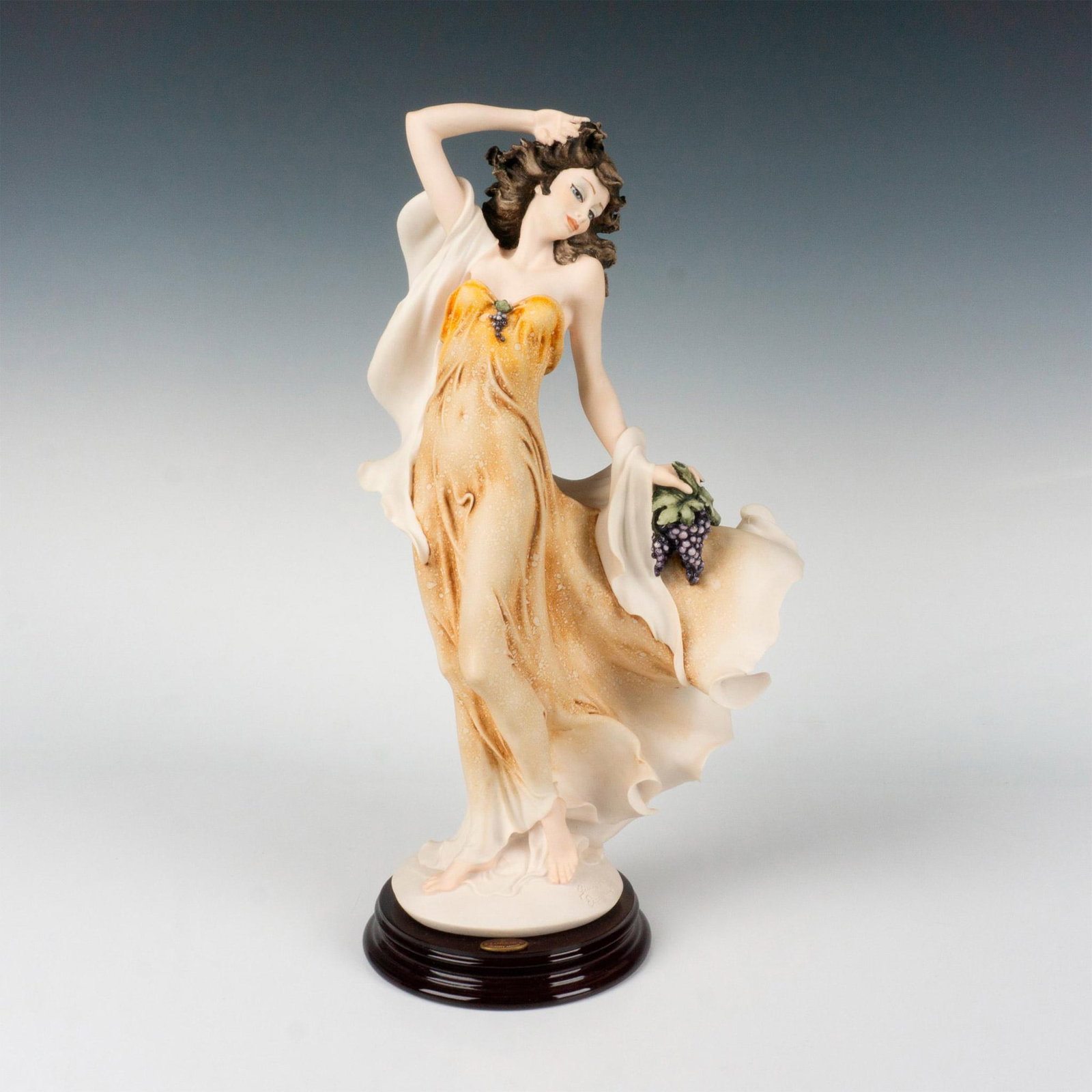 Florence Giuseppe Armani Sculpture, Autumn Harvest 1697C: Matte finished figure in style of Capodimonte of a woman in a flowing orange and cream colored dress holding grapes. Fixed to dark wood base. Giuseppe Armani impressed to base and Capodimonte backstam