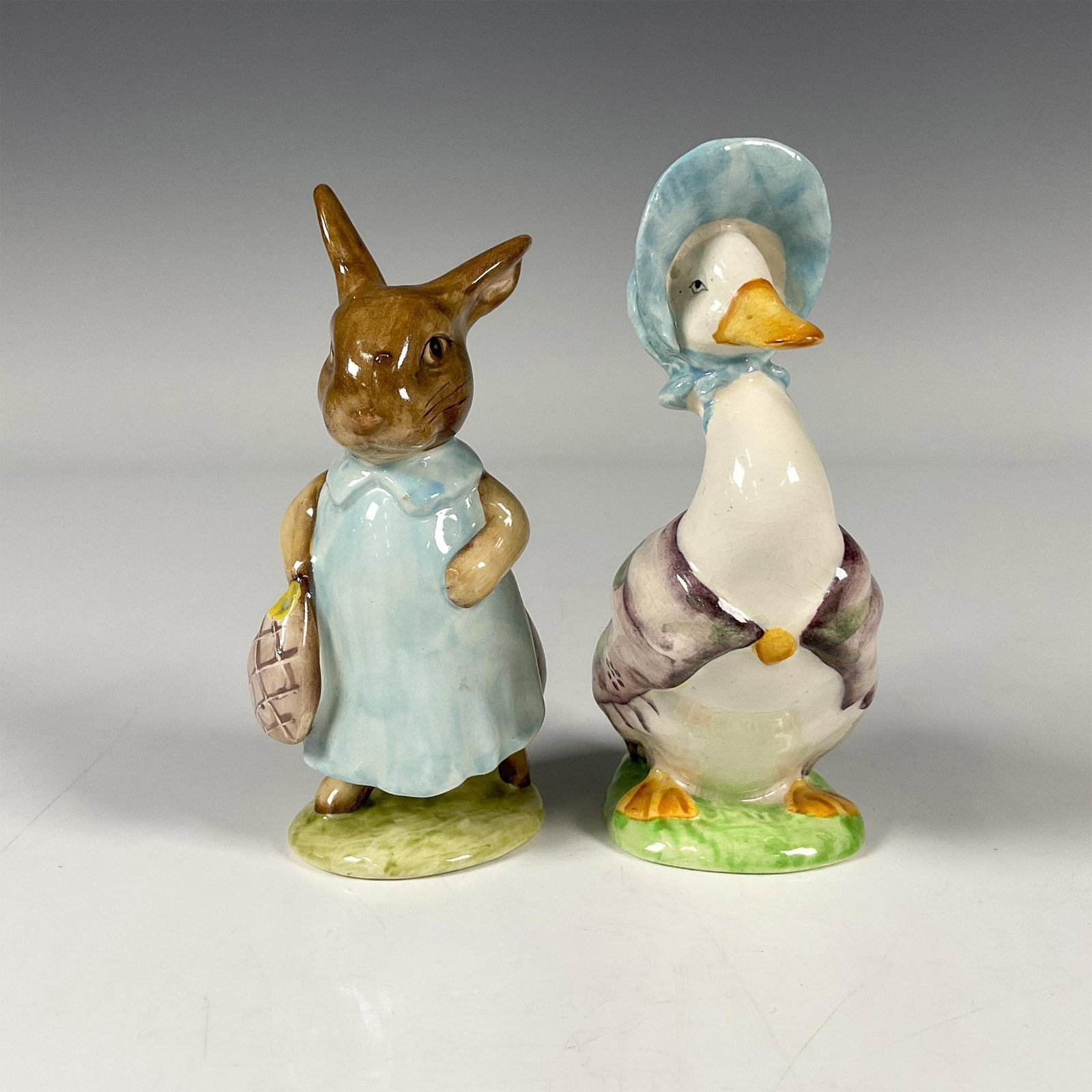 2pc Beswick Beatrix Potter Figurines, Jemima & Mrs Flopsy: Includes the characters Mrs. Flopsy Bunny in a blue dress and purple bag and Jemima Puddle-Duck wearing a purple shawl and blue bonnet. Beswick backstamp. Tallest piece dimensions: 4''H x 1.75''dia. I