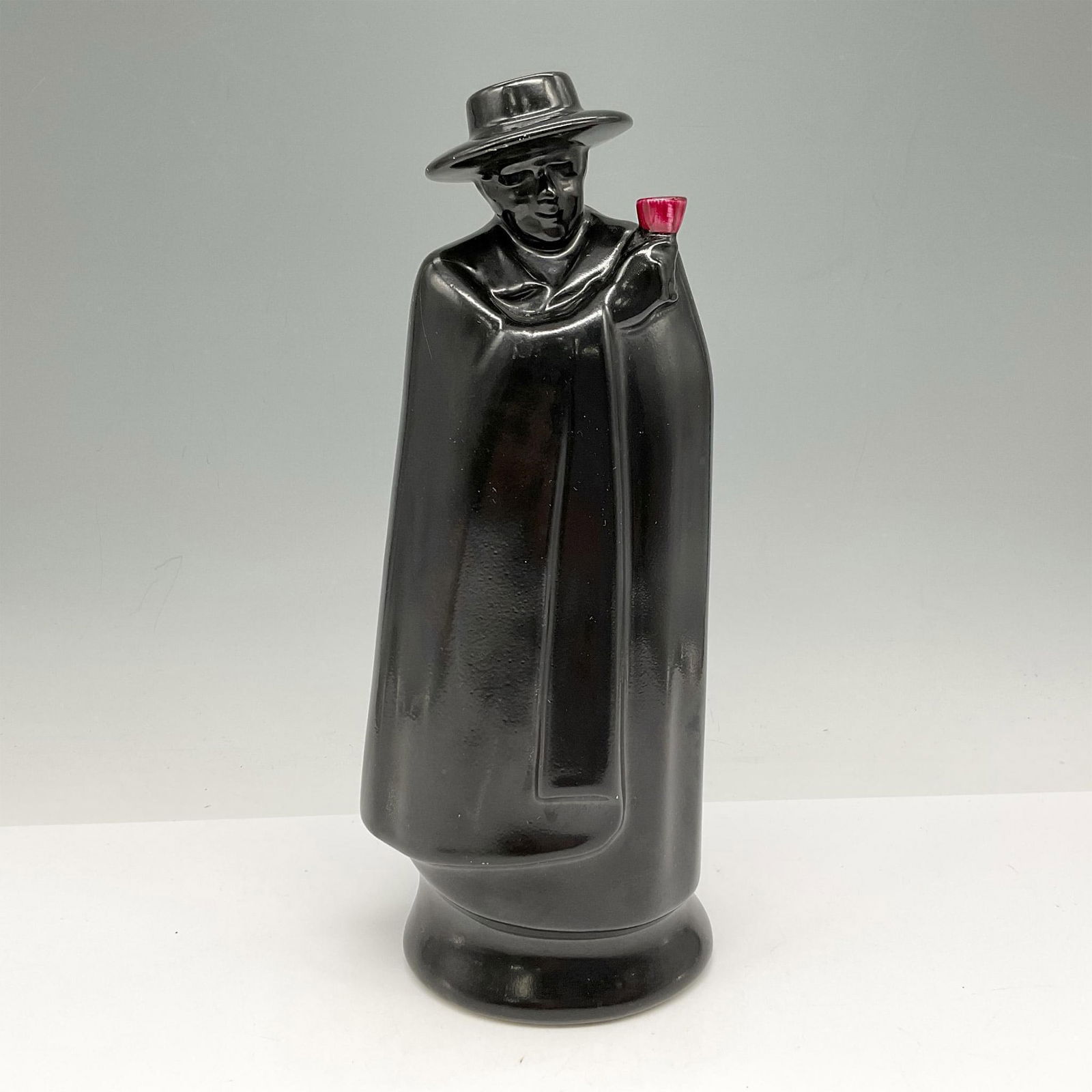 Royal Doulton Porcelain Sandeman Port Decanter: Mysterious man dressed in black cape holding a red chalice cup. Red cup is the indication that bottle is for Port. Made by Royal Doulton for Geo Sandeman & Sons of London. Royal Doulton backstamp. Iss