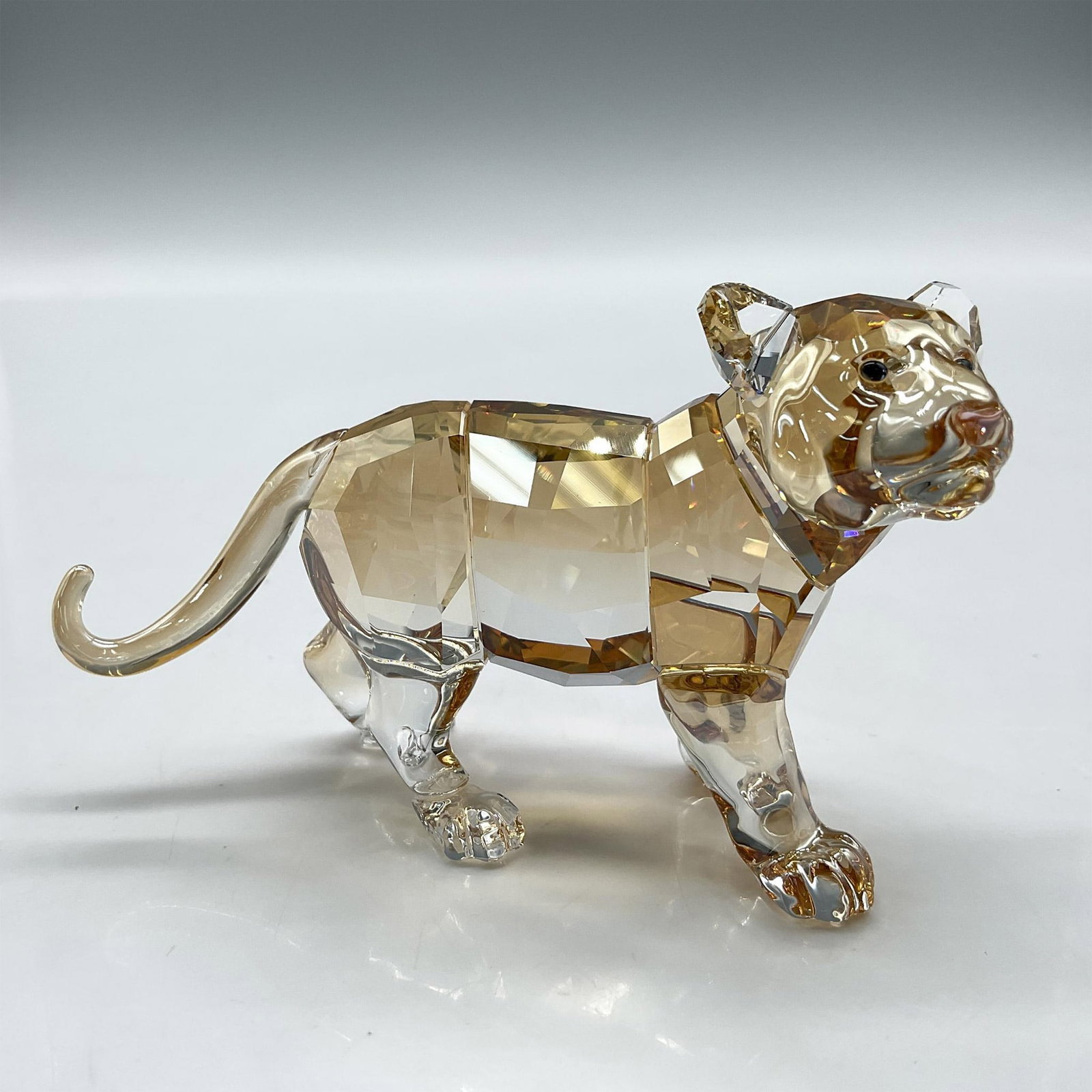Swarovski Crystal Figurine, SCS Tiger Cub Standing: Shimmers in fully facetted golden shine crystal with satin crystal stripes. Swarovski backstamp. 1016677. Item comes with original box measuring 5"L x 5"W x 4"H. Artist: Elisabeth Adamer Issued: 2010 
