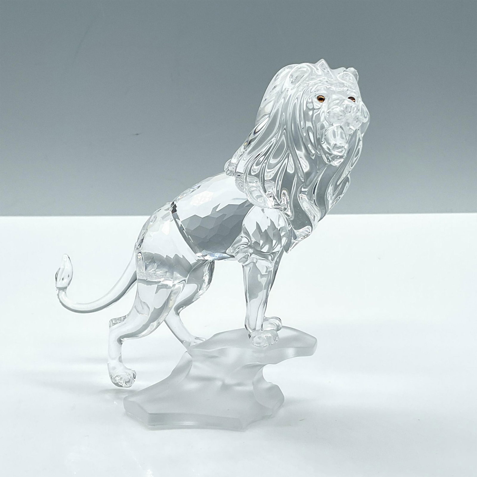 Swarovski Crystal Figurine, Lion Standing on a Rock: Part of the Rare Encounters collection, presents a faceted clear crystal lion set on a frosted rock base. Includes the original box dimensions: 5.75''L x 7.5''W x 8''H. Swarovski backstamp. Artist: Ma