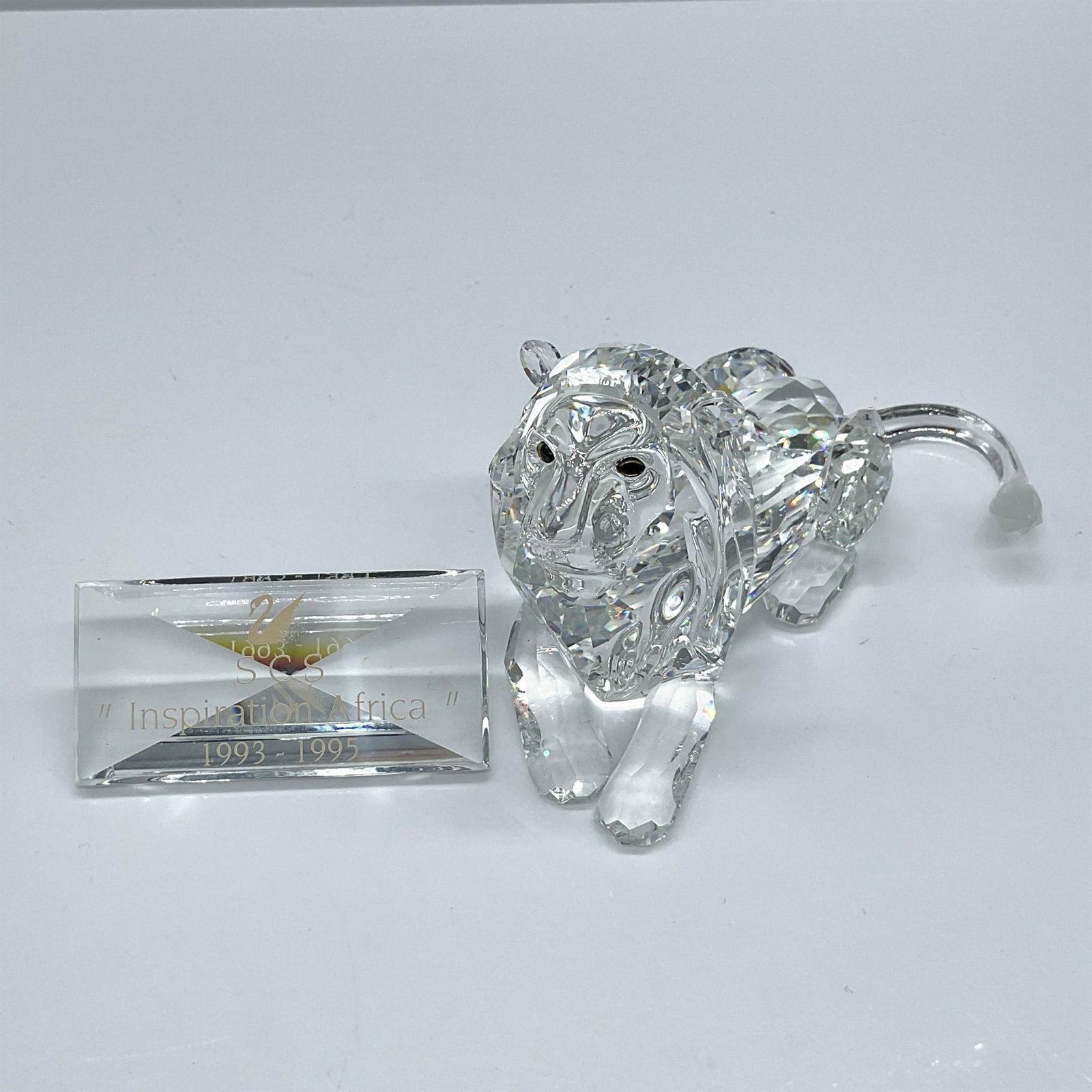 Swarovski Crystal Figurine, Inspiration Africa Lion + Plaque: From the Inspiration Africa collection. Presents this majestic animal in dazzling clear lion with frosted tail, laying serene. Accompanied by a matching clear crystal plaque. Includes the original box