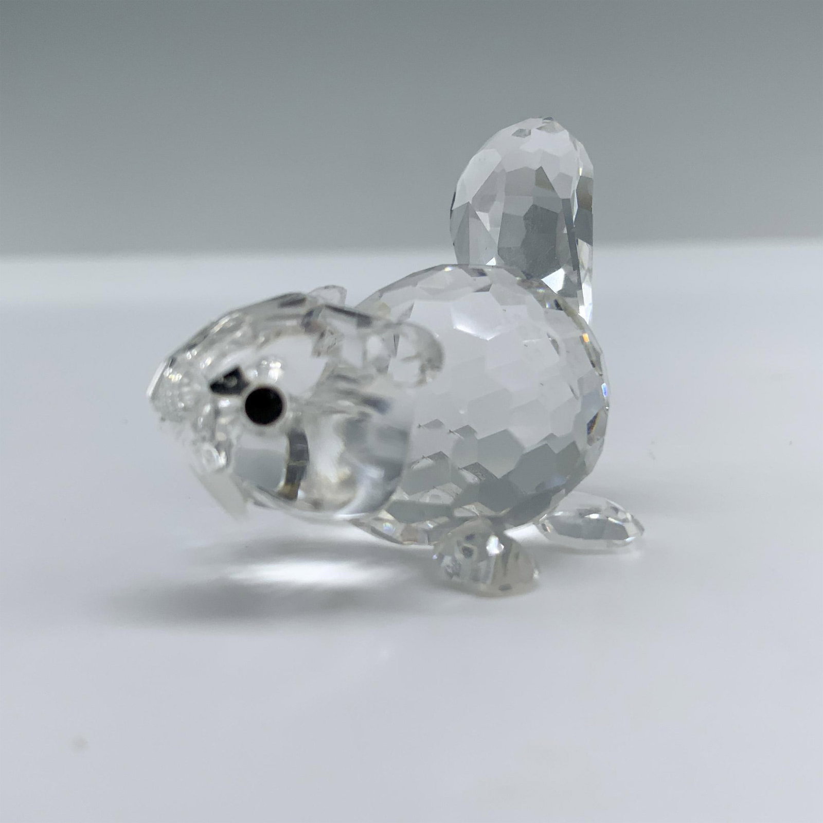 Swarovski Crystal Figurine, Baby Beaver Lying 164639: A baby beaver lying on all fours with its tail pointed upwards, displaying a face of pure innocence. Swarovski backstamp. This item has its original box. Box measures: 2.5"H x 3.25" dia. Artist: Adi S