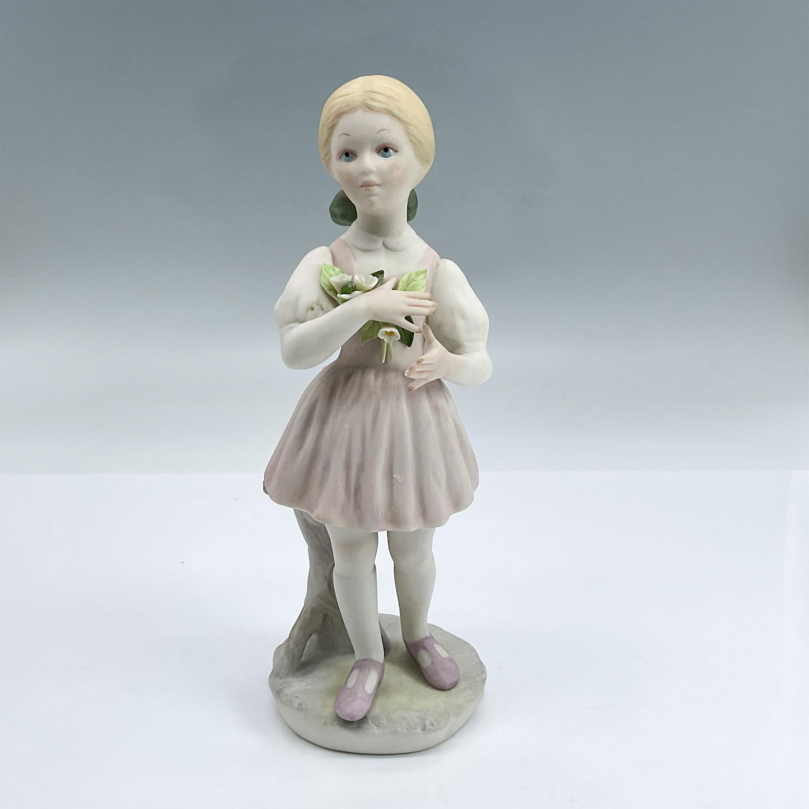 Cybis Porcelain Figurine, Heidi: Matte porcelain figure of a young girl in a pink dress holding flowers. Cybis backstamp. Dimensions: 3.25"L x 2.75"W x 8"H Manufacturer: Cybis Country of Origin: United States