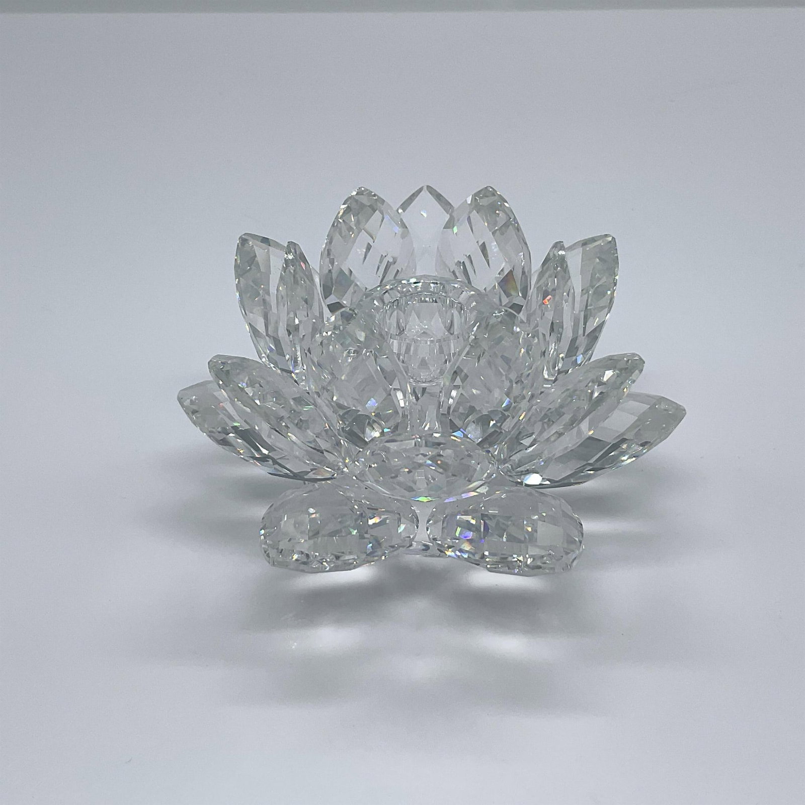Swarovski Crystal Candleholder, Waterlily - Medium: A clear crystal candleholder in a shape of a multi-petal flower. Swarovski swan mark. This item has its original box: 6"W x 4.75"H. Artist: Max Schreck Issued: 1982 - 2011 Dimensions: 3.75"W x 2.25"H 