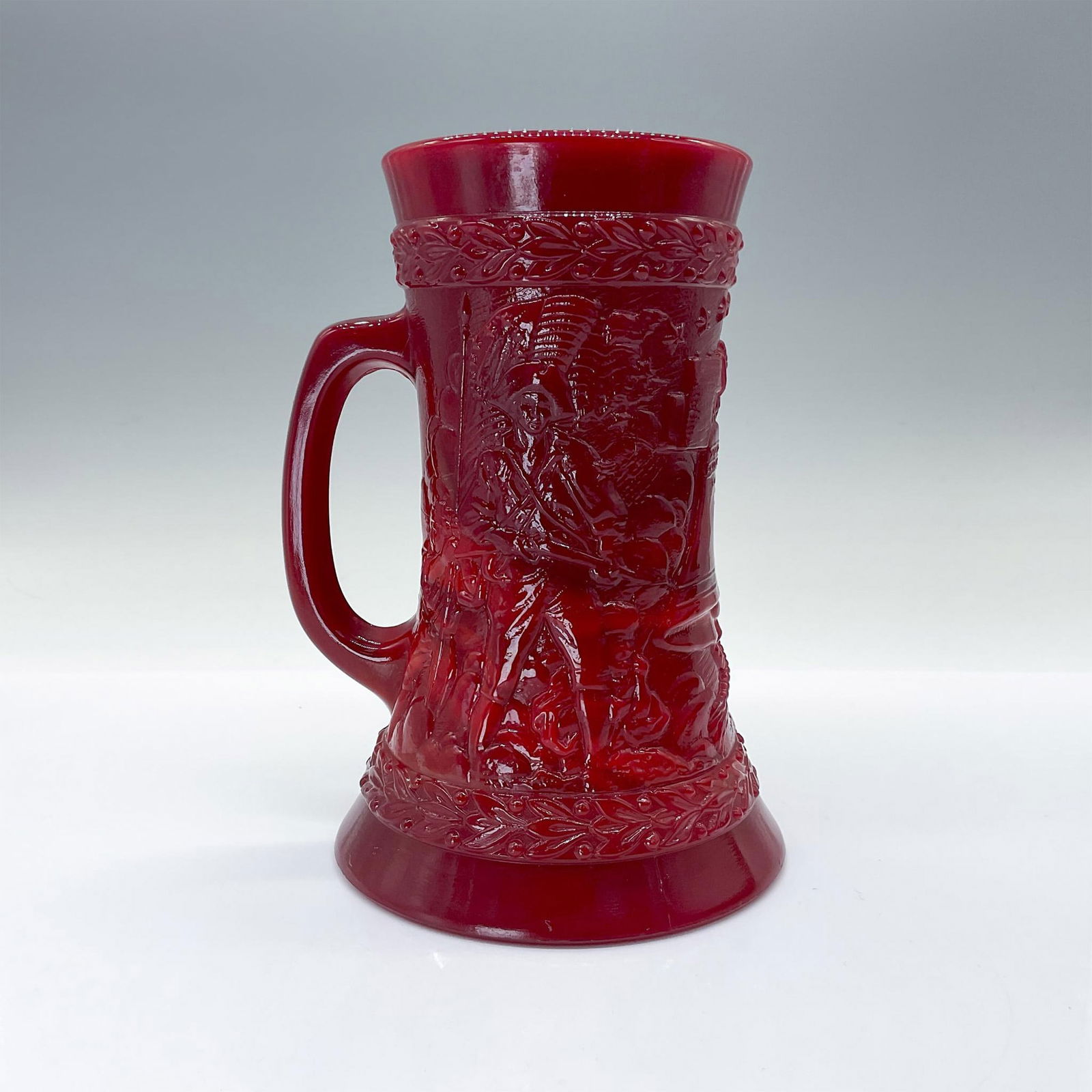 Fenton Bicentennial Red Tankard: This beautiful red glass is decorated with imprinted American scenes, adding a touch of nostalgia and charm. Issued: 1976 Dimensions: 5.25"L x 4.75"W x 6.75"H Manufacturer: Fenton Country of Origin: U