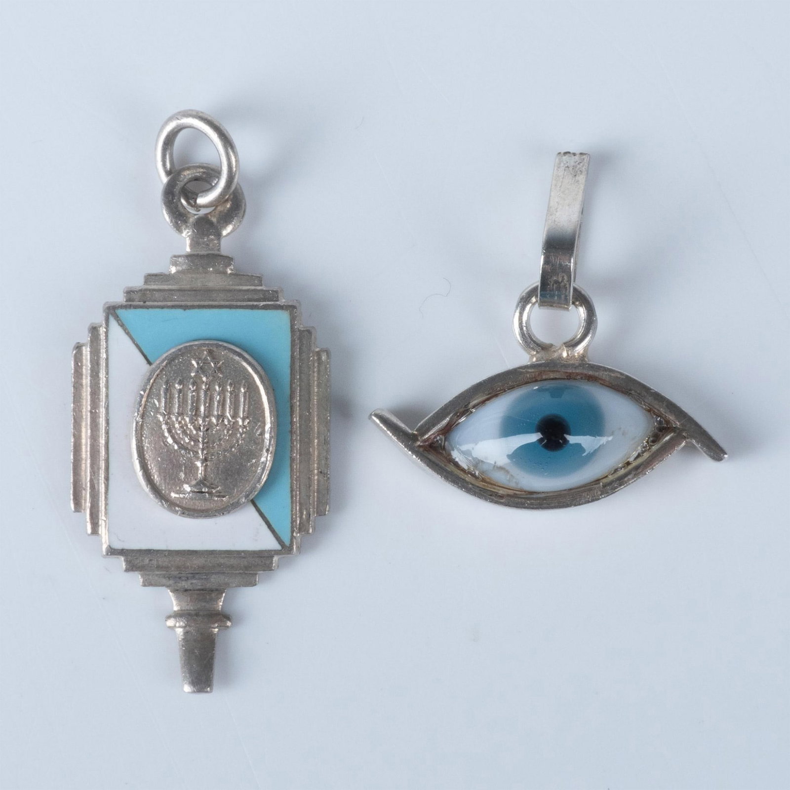 2pc Small Sterling Silver Judaica Menorah and Eye Pendants: The enameled menorah piece is marked Barr's Sterling on the back and measures approximately 1.25"L x 0.75"W. The glass eye pendant is hallmarked and stamped sterling on the back. It measures approxima