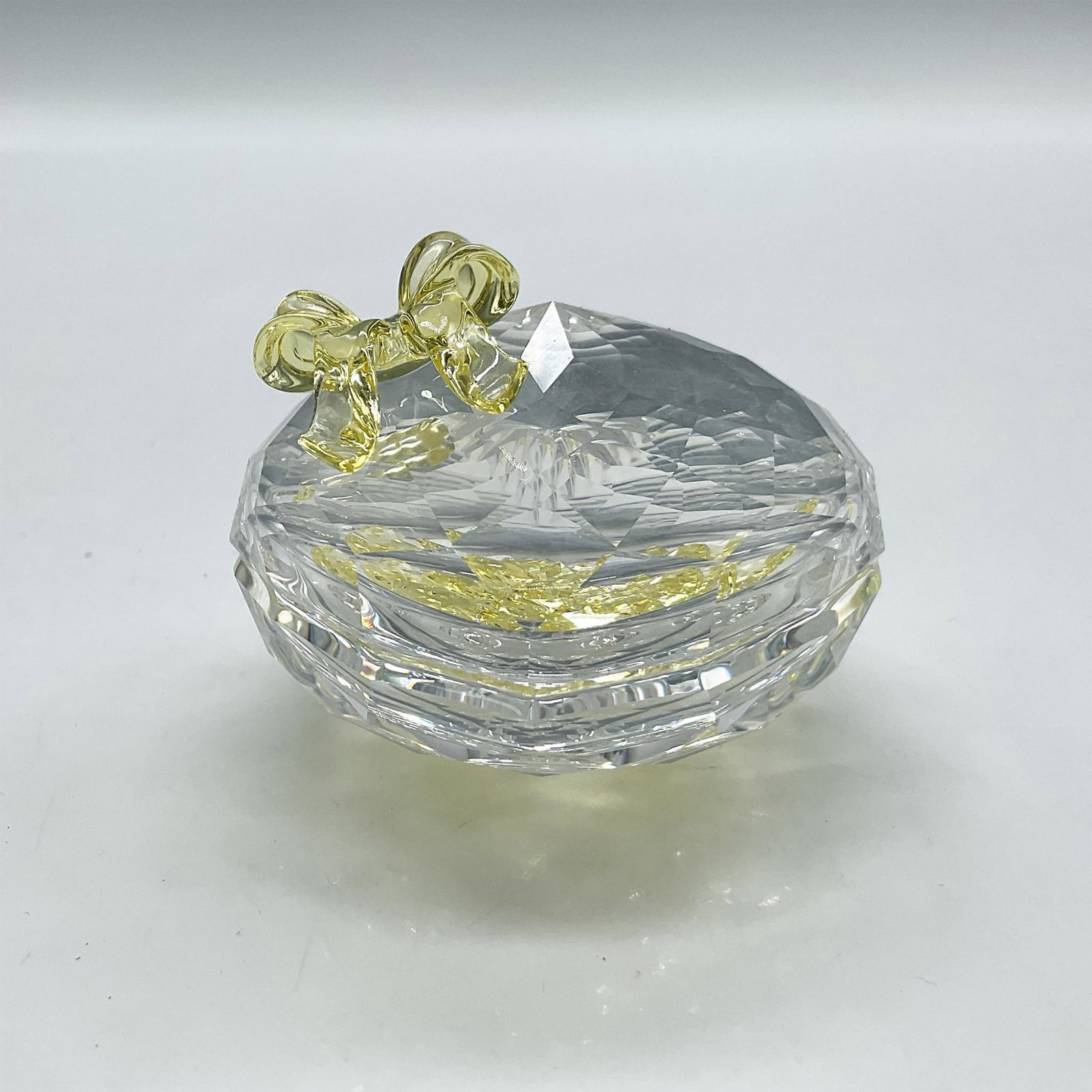 Swarovski Crystal Anna's Jewel Box: Clear crystal faceted heart shaped box with lid. Lid has yellow crystal bow. Box contains yellow crystal loose rhinestones. Swarovski backstamp. 666890. This item has its original box: 4"H x 5" dia. A