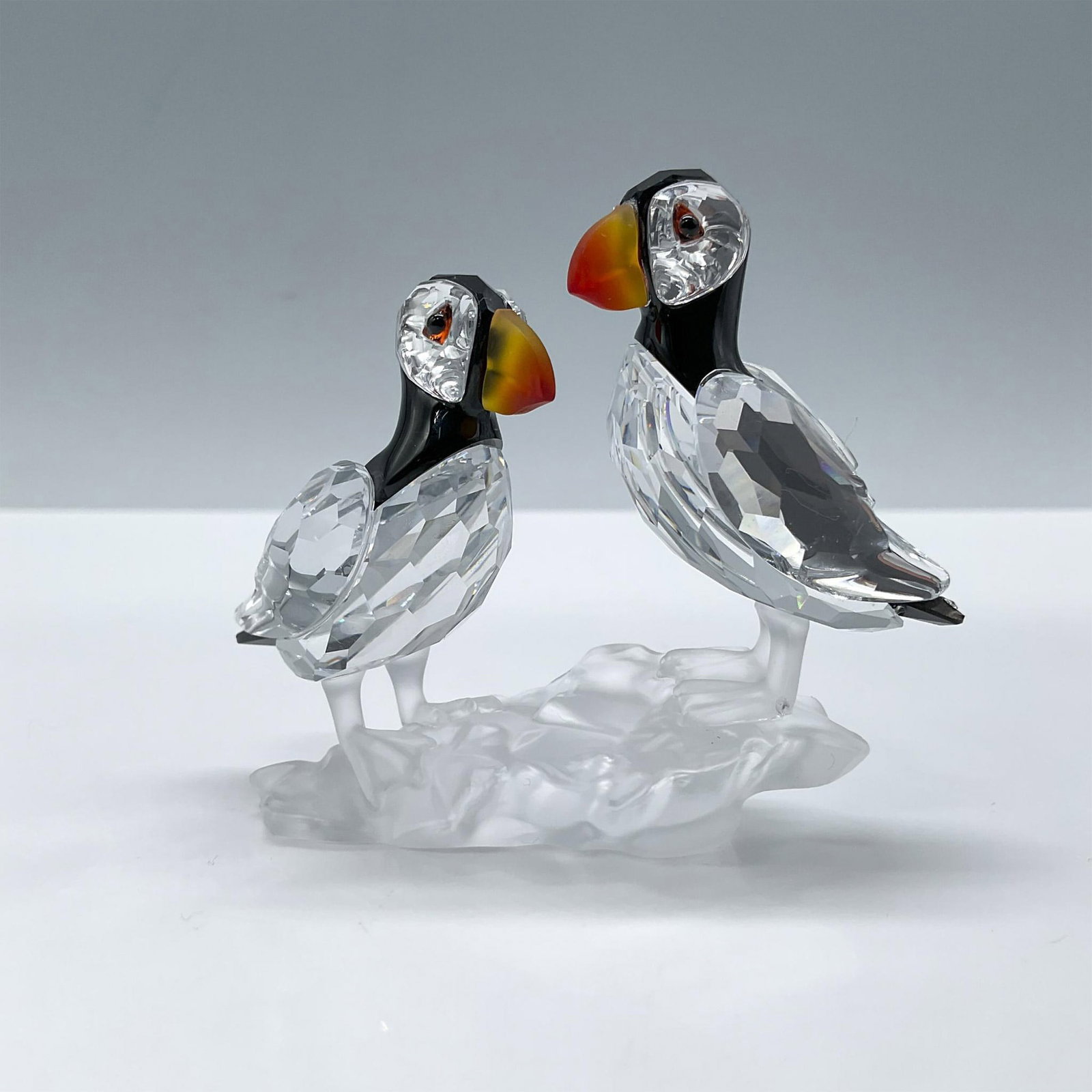 Swarovski Crystal Figurine, Puffins: From the Feathered Beauties collection. Features two lovely birds in clear and black crystal with fire opal beaks perched on a frosted crystal rock. Swarovski etched backstamp. This item has its origi