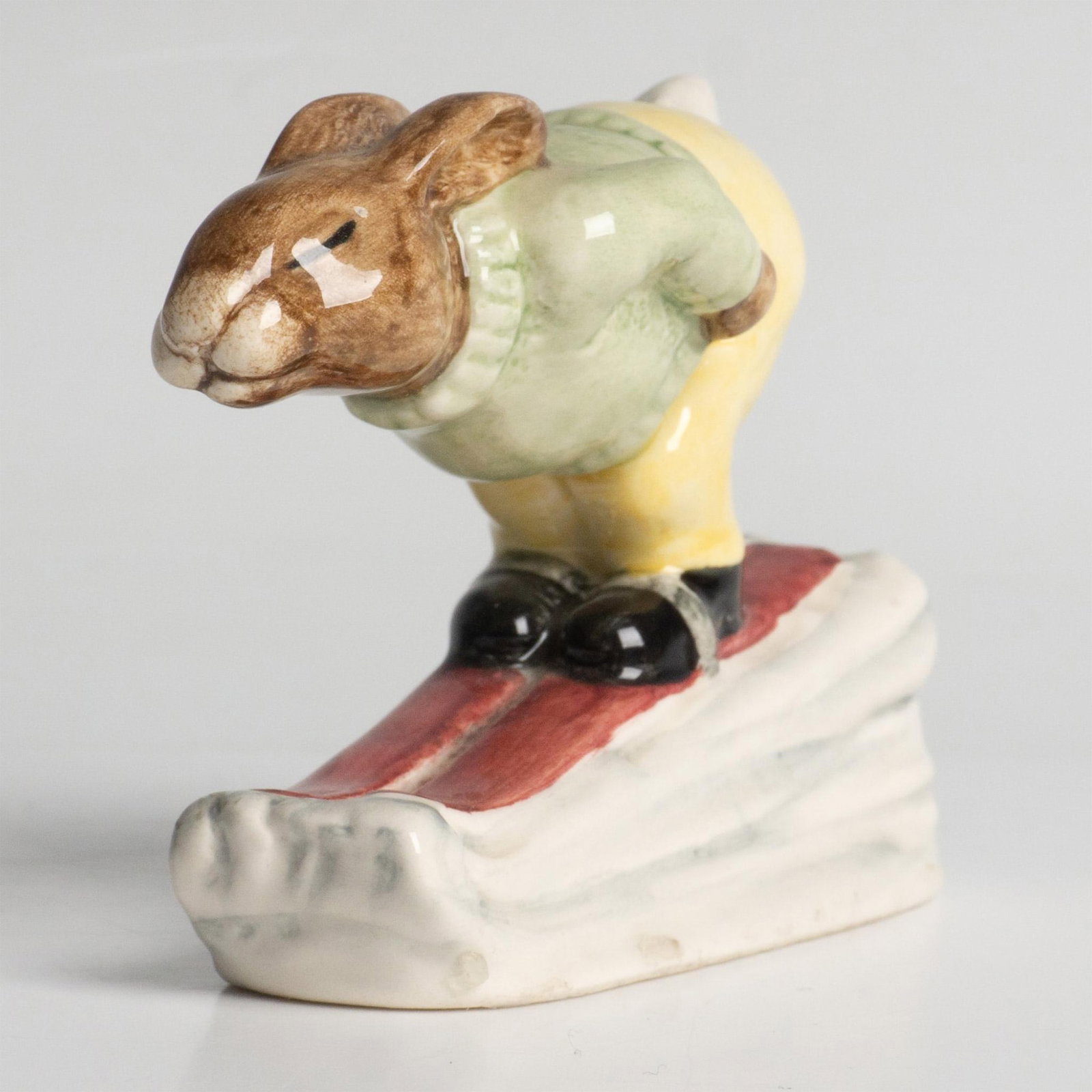 Downhill DB31 - Royal Doulton Bunnykins: A bunny skiing down a slope, wearing a green sweater and yellow pants. Royal Doulton backstamp. Artist: H. Sales Issued: 1985 - 1988 Dimensions: 2.5"H Manufacturer: Royal Doulton Country of Origin:</