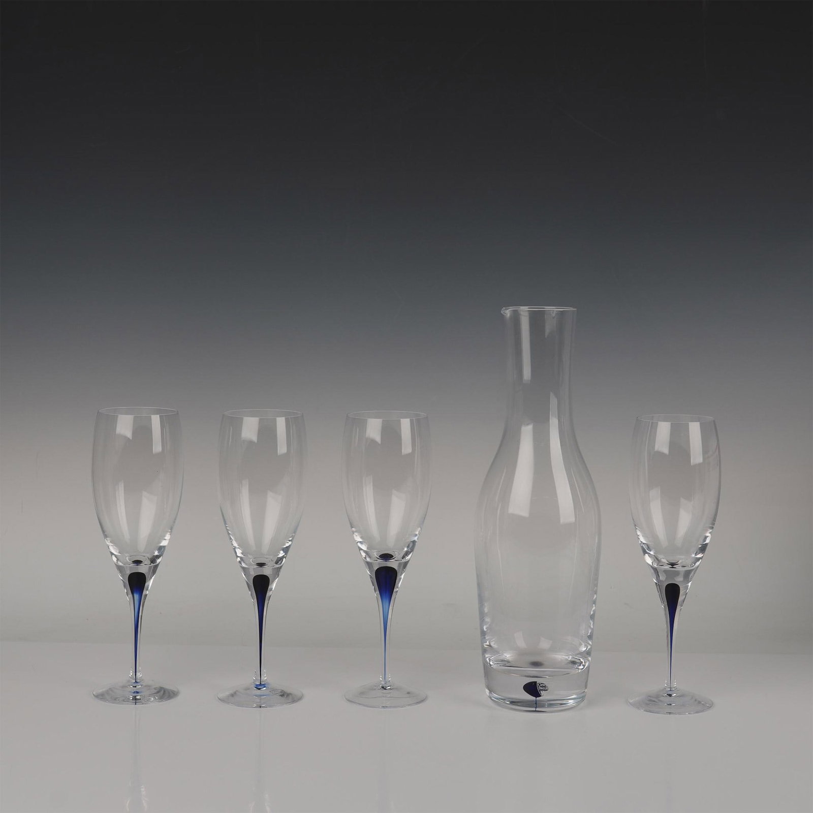 5pc Orrefors Wine Glasses and Carafe, Intermezzo Blue: Four wine glasses and one carafe, each adorned with a sophisticated deep blue accent. Orrefors Sweden manufacturing sticker. Dimensions of the largest item: 12"H x 3.75" dia. Artist: Erika Lagerbielke
