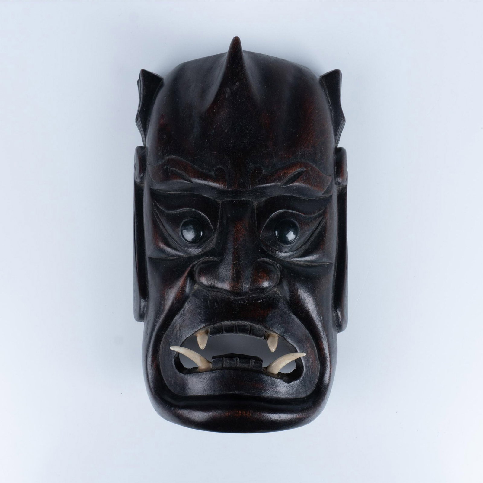 Japanese Carved Lacquered Wall Mask: Hand carved mask colored as burnished wood with beaded eyes and resin shaped teeth. Issued: 20th century Dimensions: 10.75"L x 7"W x 4"H