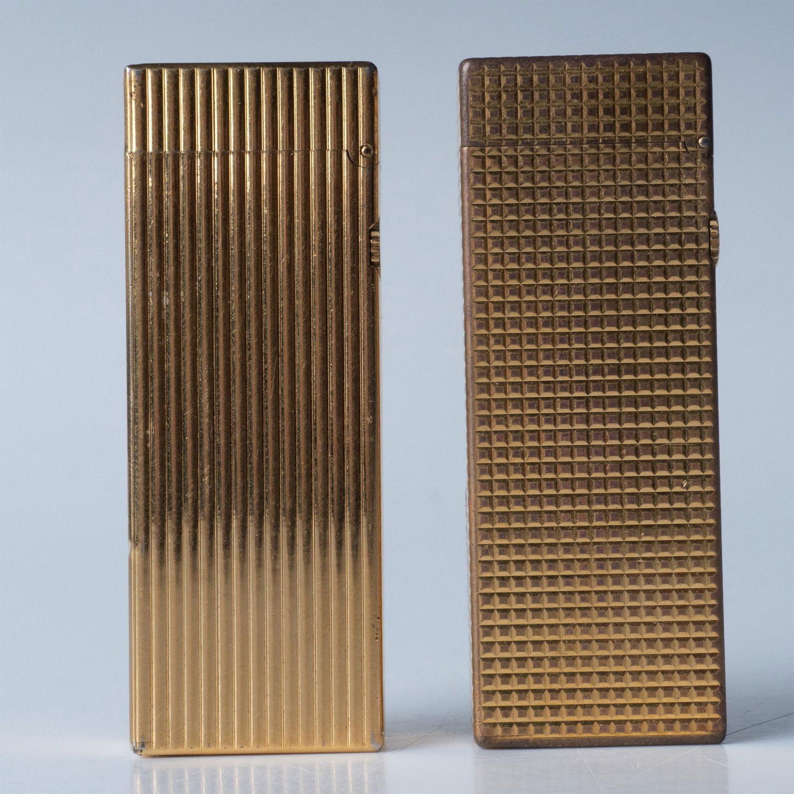 2pc Dunhill Vintage Textured Golden Rollagas Lighters: These gold metal lighters are Swiss-made with Dunhill hallmarks. Issued: 20th c. Dimensions: 1"L x 0.5"W x 2.5"H Manufacturer: Dunhill Country of Origin: England