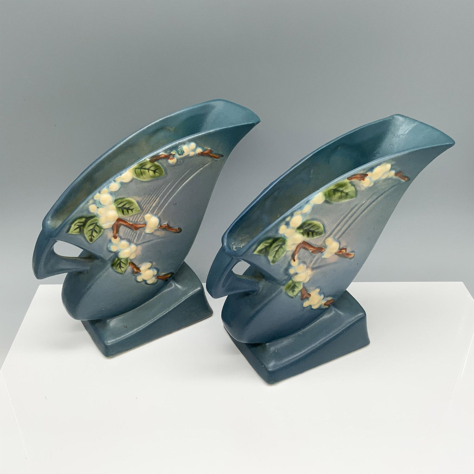 Pair of Roseville Snowberry Blue Vases: Enchanting pottery duo of flower holders with a branch design. Roseville backstamp. Issued: 1940s Dimensions: 8.5"L x 3.5"W x 7.5"H Manufacturer: Roseville Country of Origin: United States