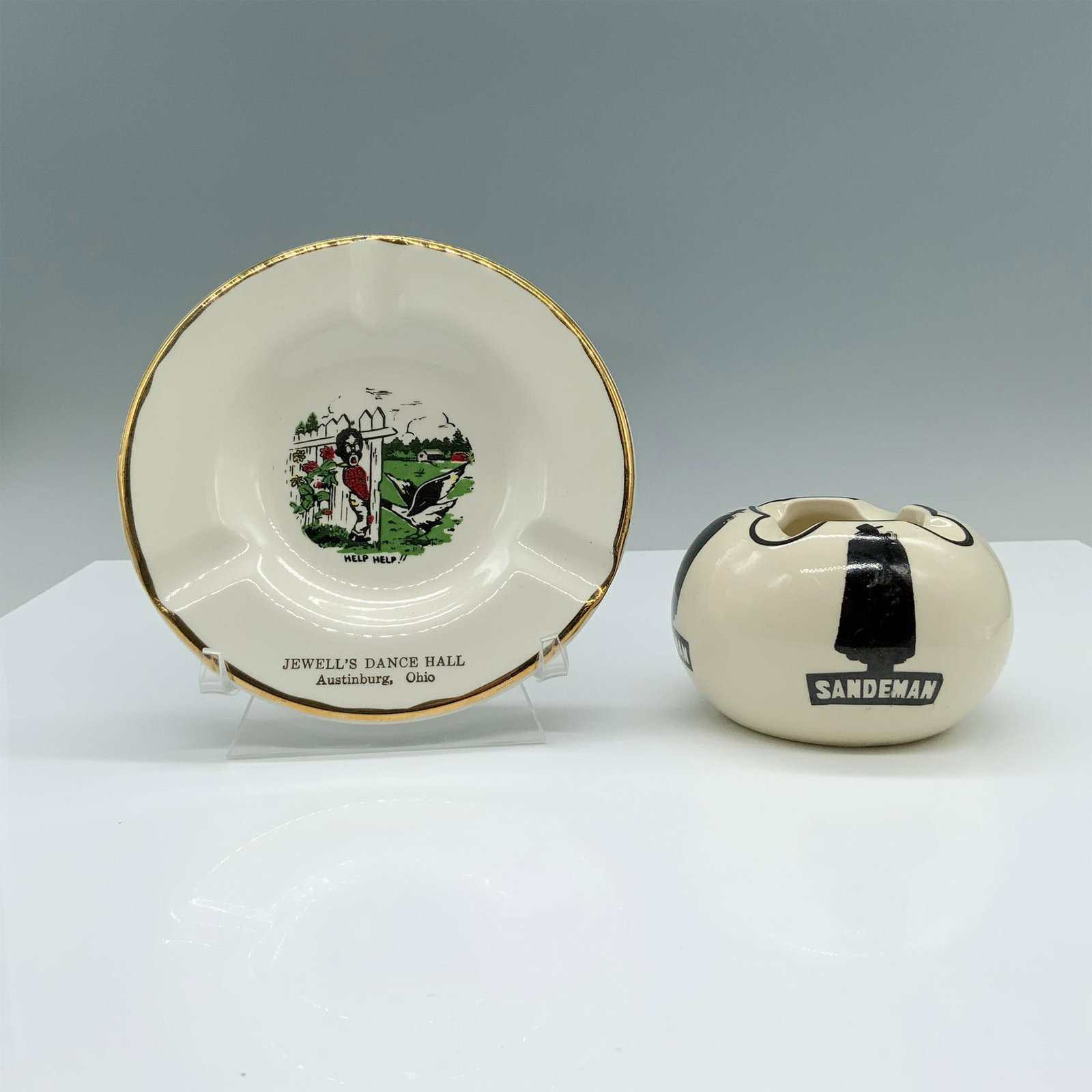 2pc Sandeman Ashtray and The Sabina Line Dance Hall Plate: A cream colored ashtray with black accents featuring the Sandeman logo silhouette, alongside a white plate with gold trim depicting a man being attacked by a goose through a fence. Marked England on a