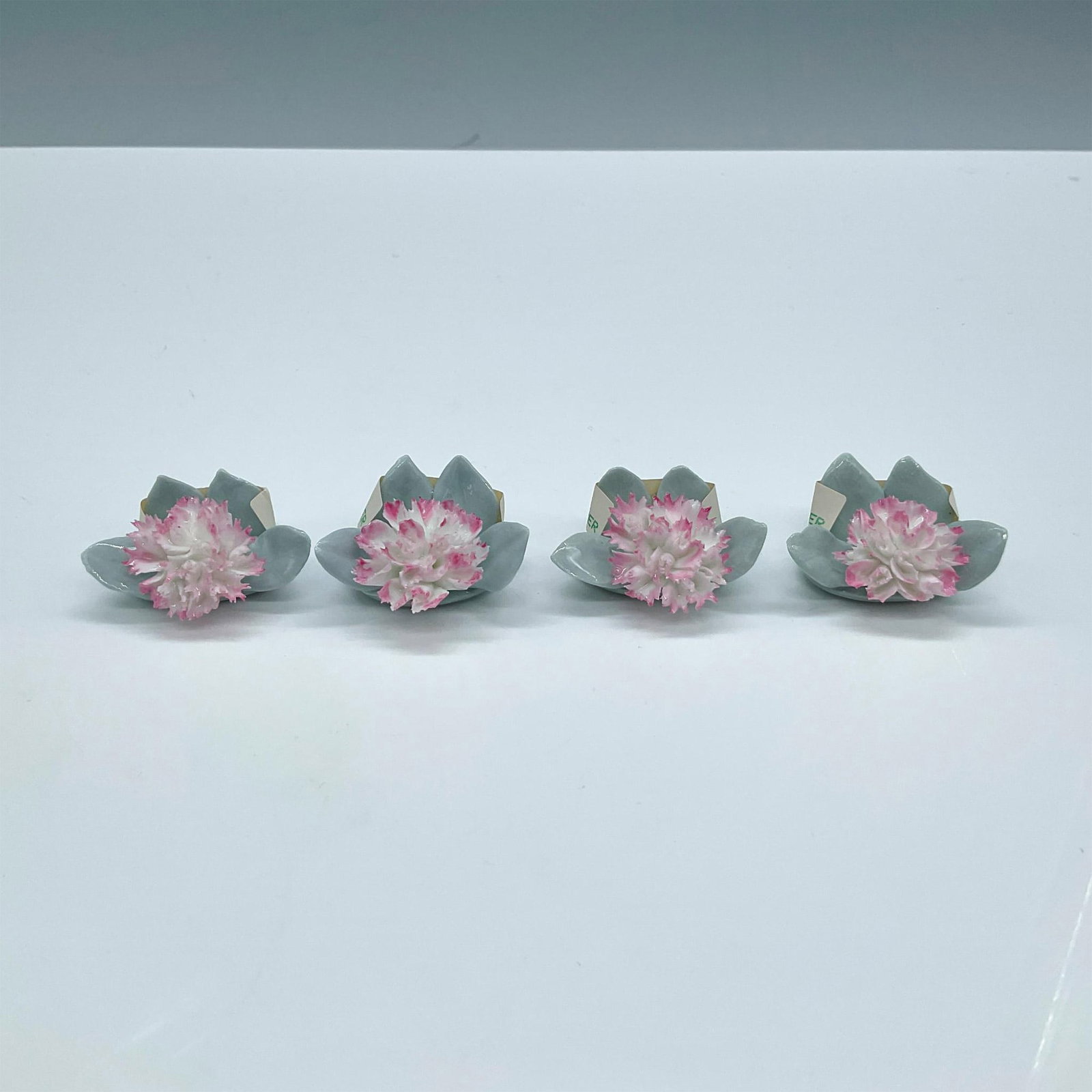 4pc Royal Doulton Bone China Place Card Holders, Carnation: Delicate pink flowers, elegantly designed to hold cards with grace and charm, adding a touch of floral beauty to any display. Includes the original box, dimensions: 3''L x 3''W x 4''H. Royal Doulton b