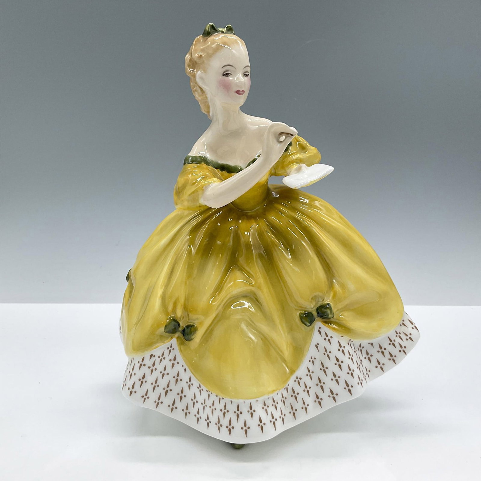 The Last Waltz HN2315 - Royal Doulton Figurine: Depicts a charming girl in a yellow dress, adorned with a white and gold decorated skirt and accented with green details. Royal Doulton backstamp. Artist: Mary Nicoll Issued: 1967-1993 Dimensions: 5''