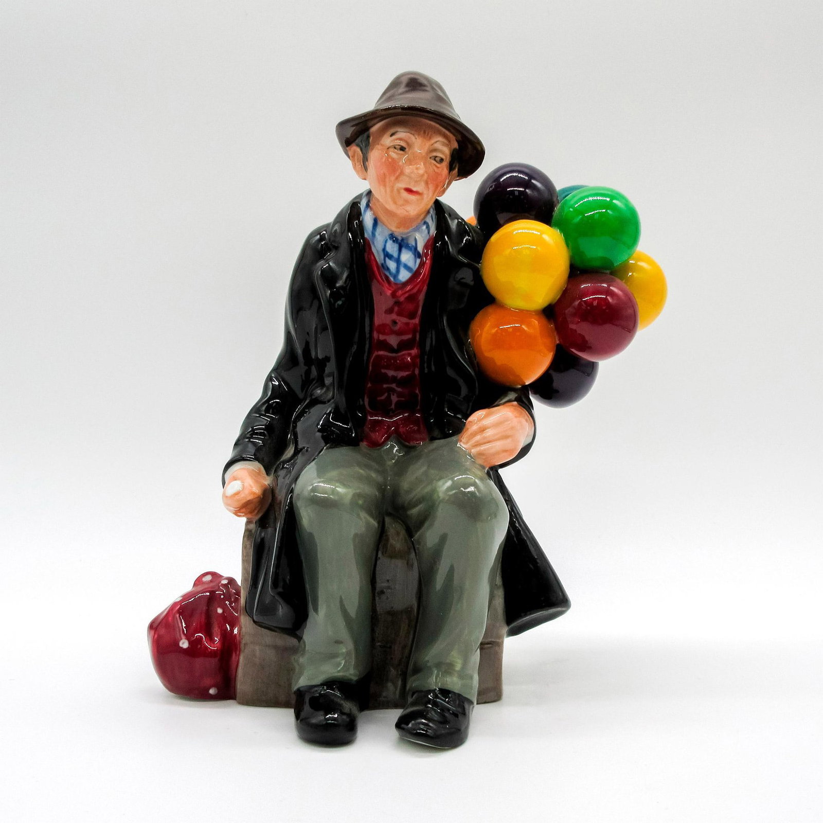 Balloon Man HN1954 - Royal Doulton Figurine: Seated figure of a man with balloons. Black and burgundy coloration. Royal Doulton backstamp. This item has no reserve. Artist: Leslie Harradine Dimensions: 4.25" L x 6.25" W x 7" H Manufacturer: Roya