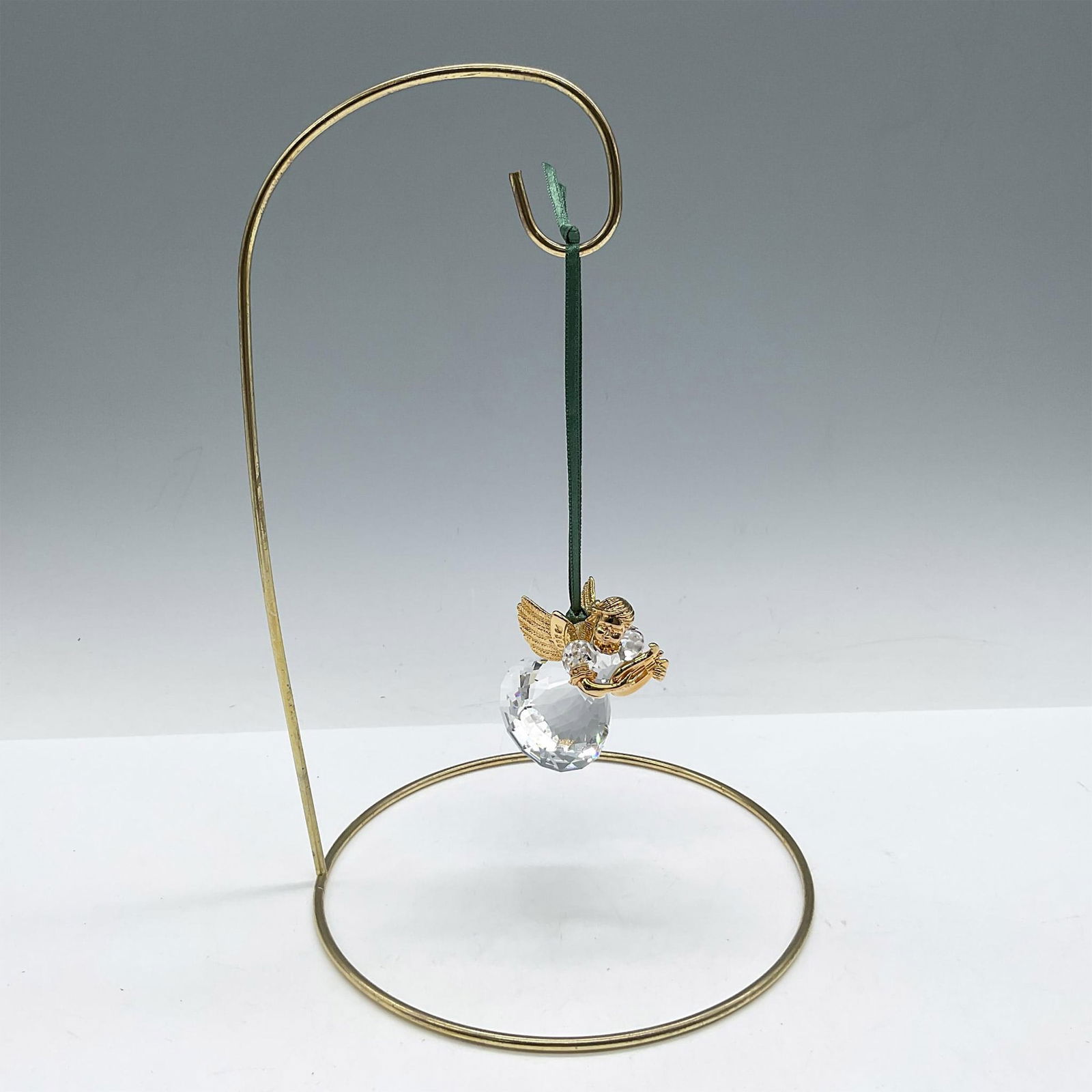 Swarovski Crystal Memories, Angel Ornament with Harp: Limited edition series of Angels for the Christmas Memories series. Designed with gilded head, wings, arms and legs wearing a faceted crystal dress playing a harp. Green satin ribbon provided for hang