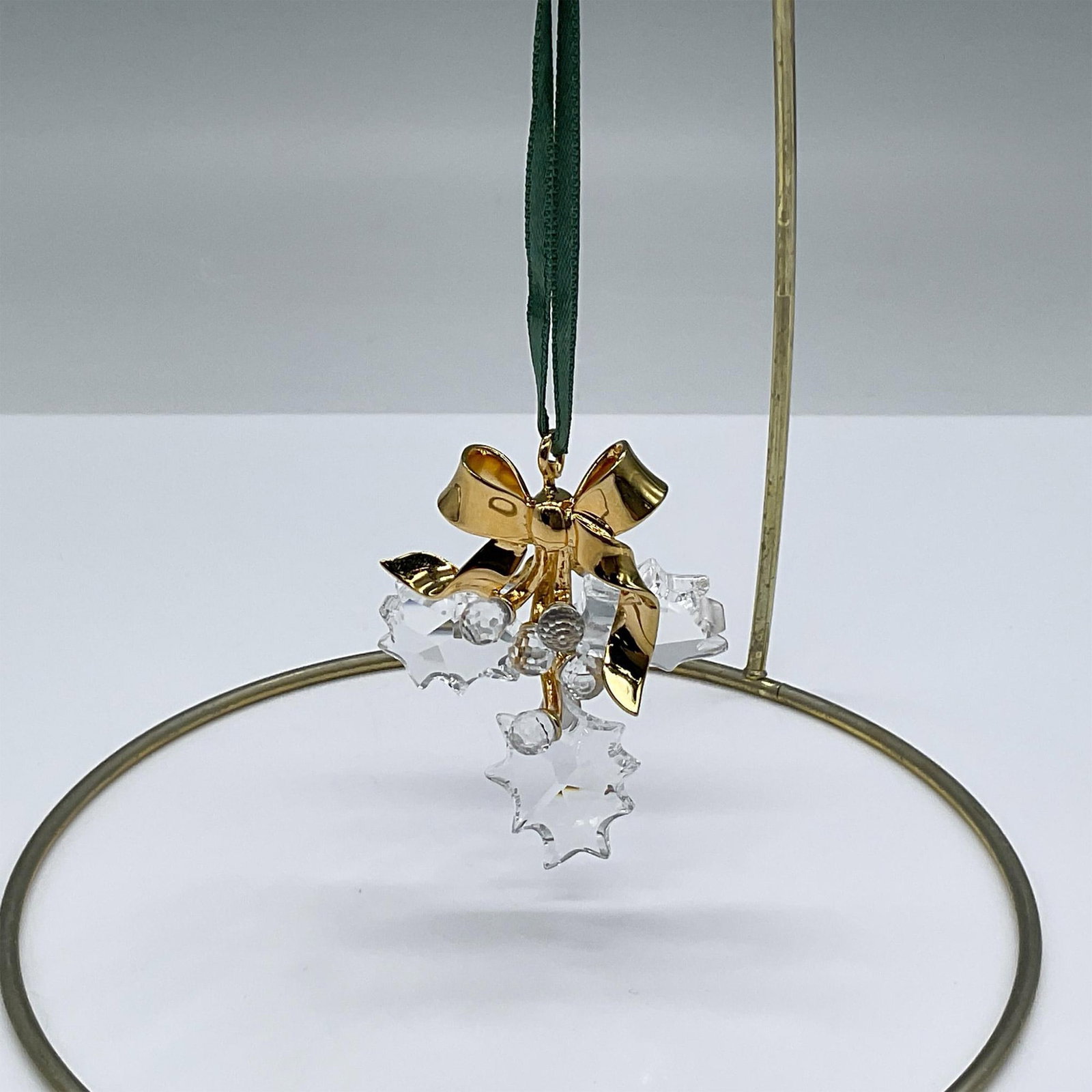 Swarovski Christmas Memories, Holly: This beautiful Christmas ornament is accented with a gold bow and hangs from a green ribbon. It has three holly leaves and five detailed berries. Swarovski backstamp on bow. This item has its original