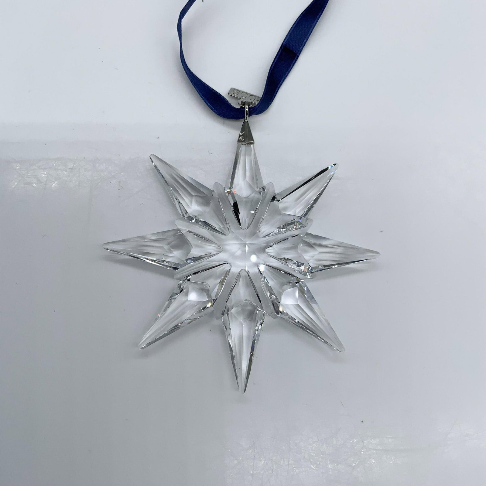 Swarovski Crystal 2009 Christmas Ornament 983702: This beautiful Christmas ornament was crafted from faceted clear crystal with silver metal and a blue ribbon. Swarovski hallmark. The triangular box measures 5.75"L x 6.5"W x 1.25"H. Artist: Elke Kuma