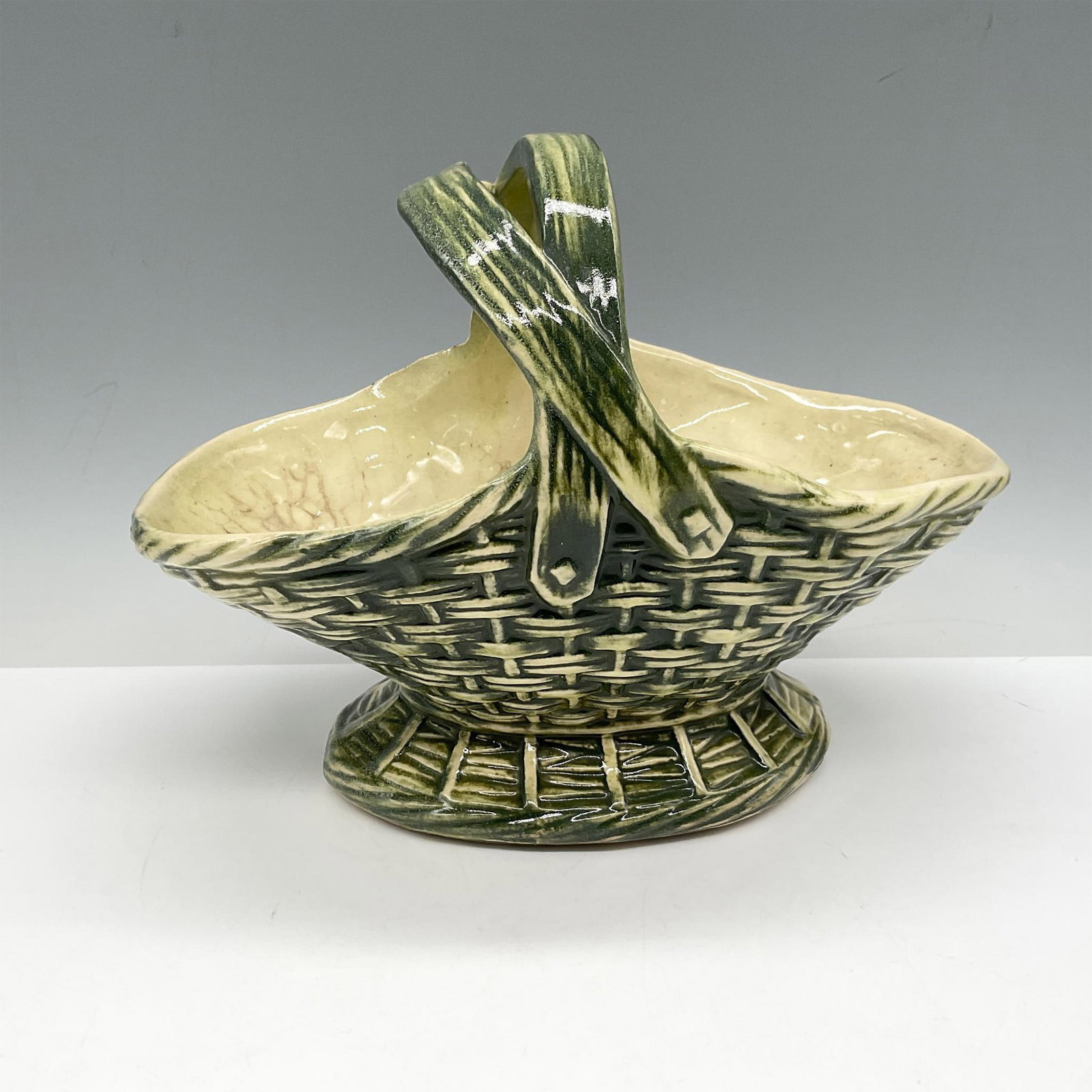 McCoy Ceramic Pottery, Basket: Glossy green pottery styled as a woven basket with handles. McCoy raised mark. Issued: 20th century Dimensions: 10"L x 5"W x 6"H Manufacturer: McCoy Country of Origin: United States