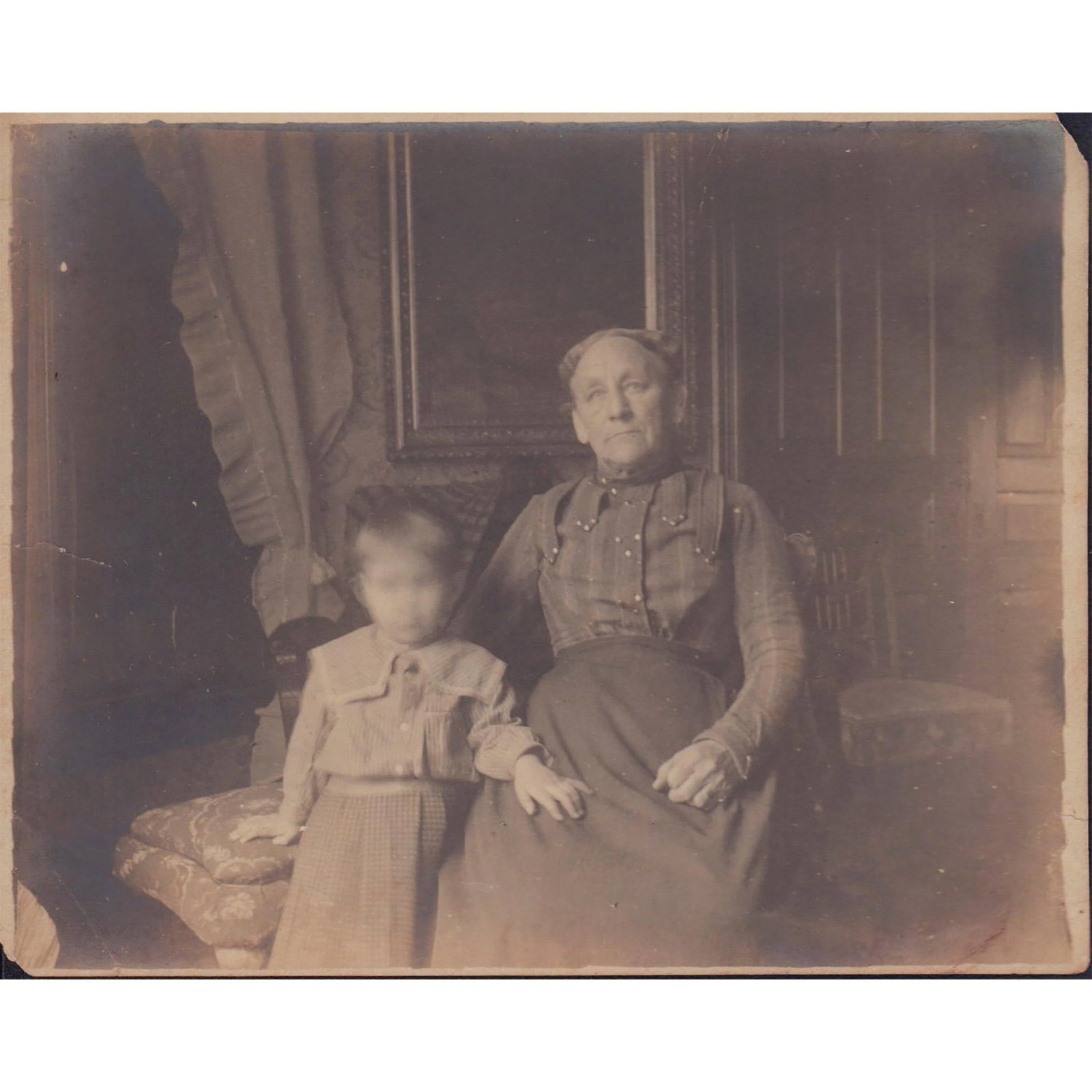 Antique Black and White Group Photo: A small indoor photo of a woman and a child posing for the camera. The child's face is blurred on purpose Dimensions: 5"W x 4"H