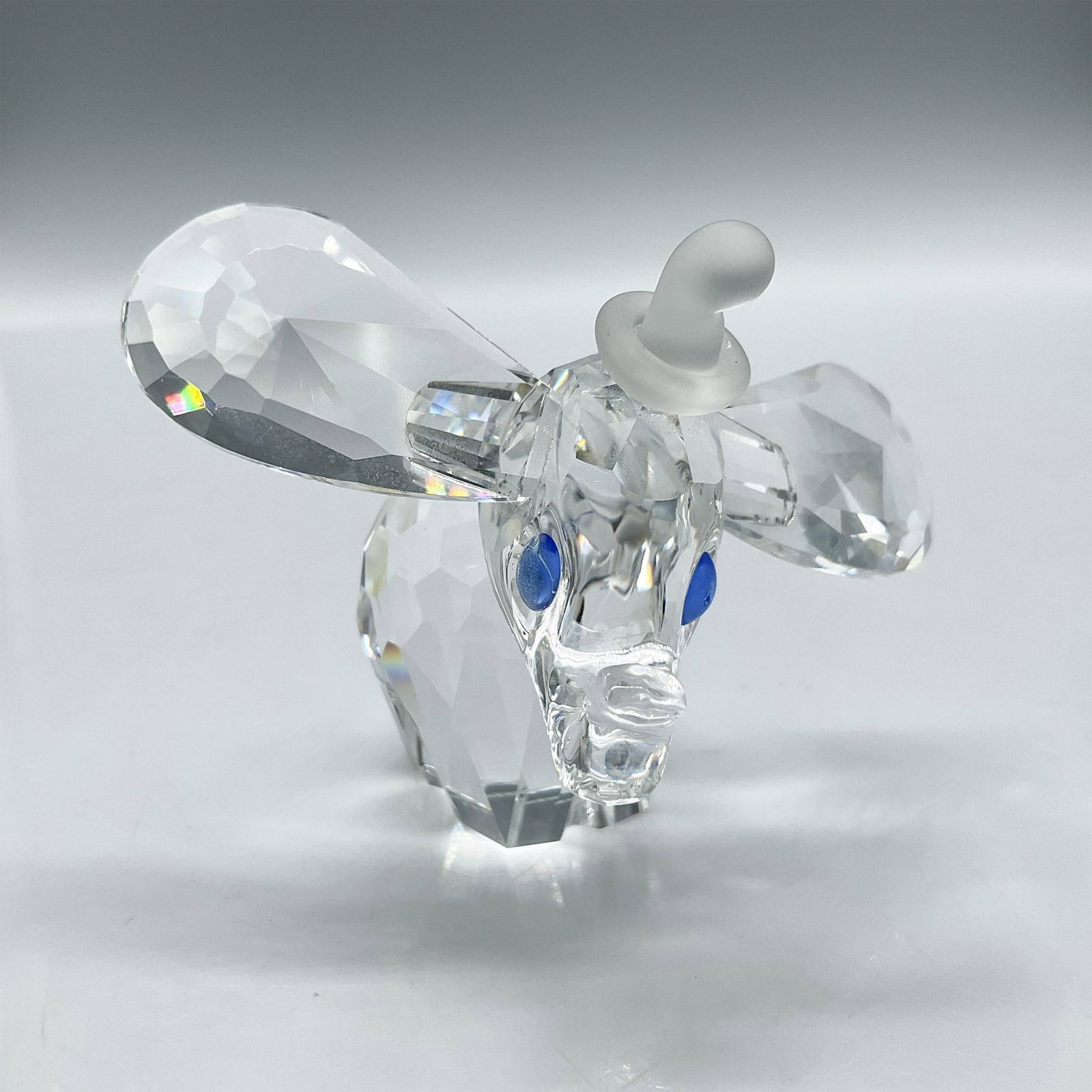 Swarovski Silver Crystal Figurine, 1993 Dumbo Blue Eyes: Clear crystal figure with large ears, blue crystal eyes, trunk raised and frosted tail wearing a frosted hat. Swarovski backstamp. 7640NR100. This item has its original box: 6"H x 5" dia. Artist: Team