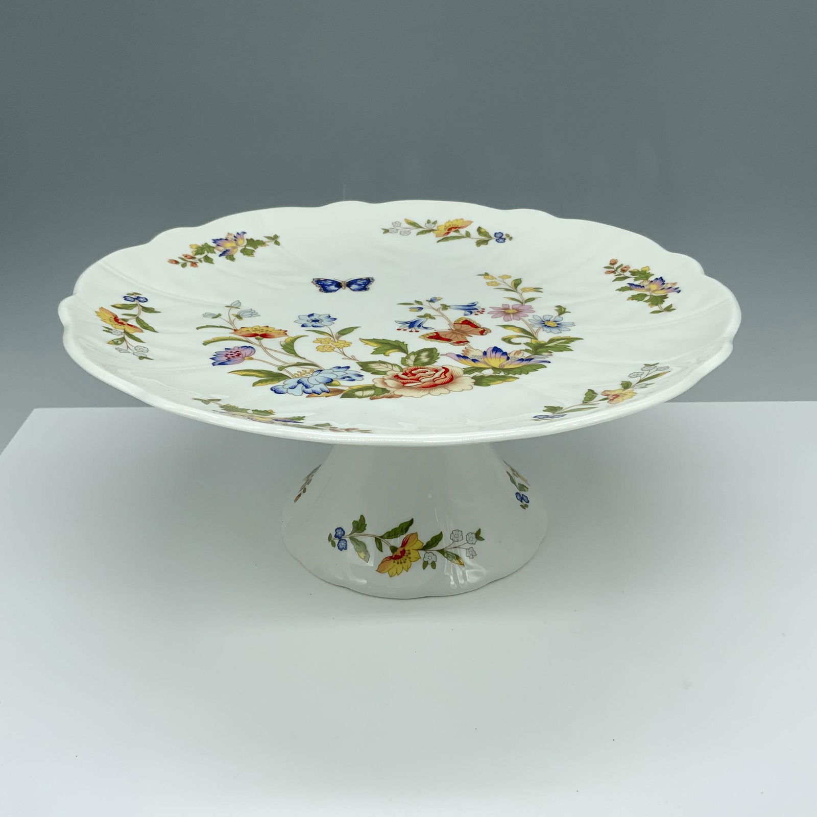 Aynsley Bone China Cottage Garden Pedestal Cake Stand: Gorgeous serving tray decorated with florals and butterflies that is used to display your pastries. Aynsley backstamp. Issued: 20th century Dimensions: 4.5"H x 10.25" dia. Manufacturer: Aynsley Countr