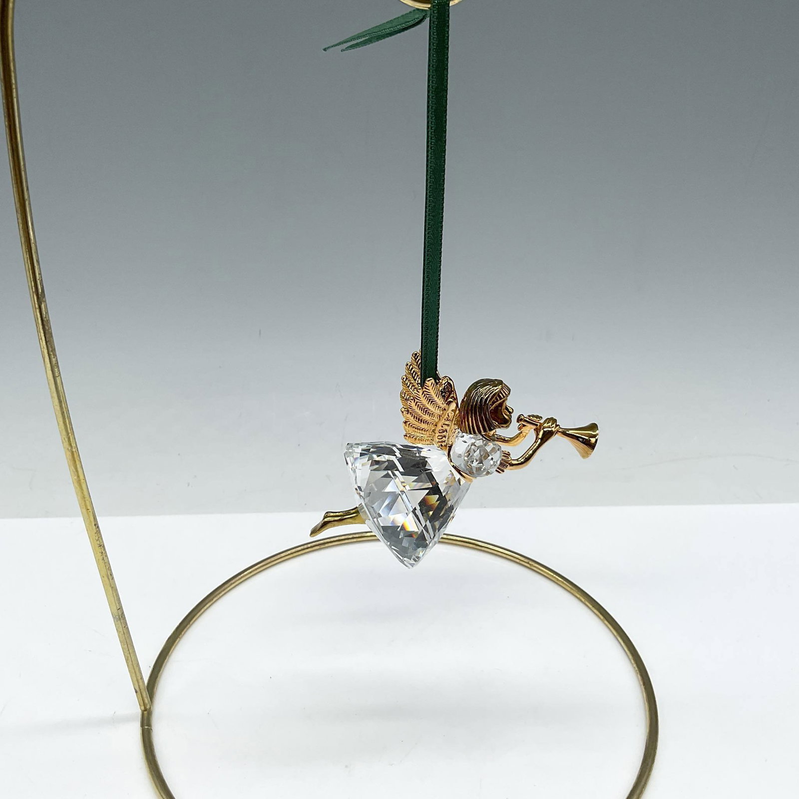Swarovski Christmas Memories Ornament, Angel with Horn: Limited edition series of Angels for the Christmas Memories series. Designed with gilded head, wings, arms and legs wearing a faceted crystal dress blowing a gilded horn. Green satin ribbon provided f