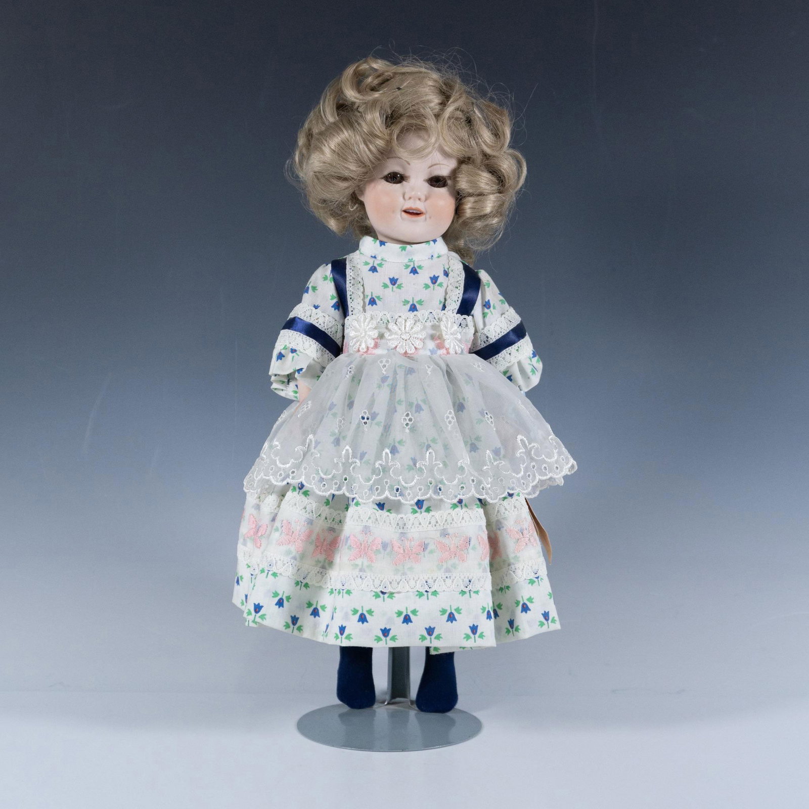 Shirley Temple Porcelain Doll in White Dress: Charming figure of a young beloved Hollywood actor wearing a lacy dress. Includes a Debbie Hawk tag and a button that says An Original Shirley Temple Doll as well as a metal stand. Dimensions: 7"L x 8
