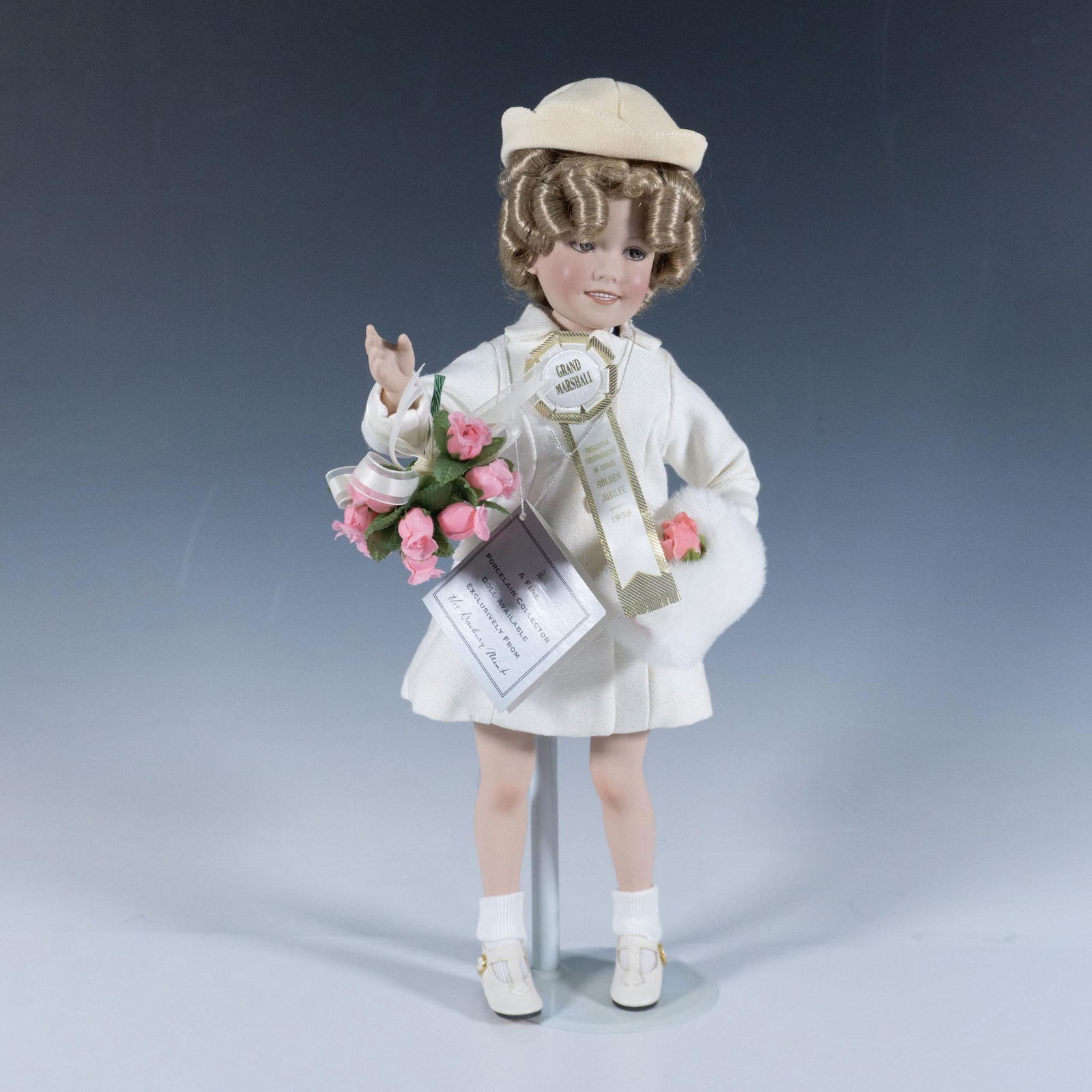 Danbury Mint Porcelain Shirley Temple Littlest Grand Marshal: Styled in winter coat with muff and her curly blonde hair bouncing under her cap. One hand holds a bunch of roses for the Pasadena Tournament of Roses Golden Jubilee 1939. Signed by artist with emboss
