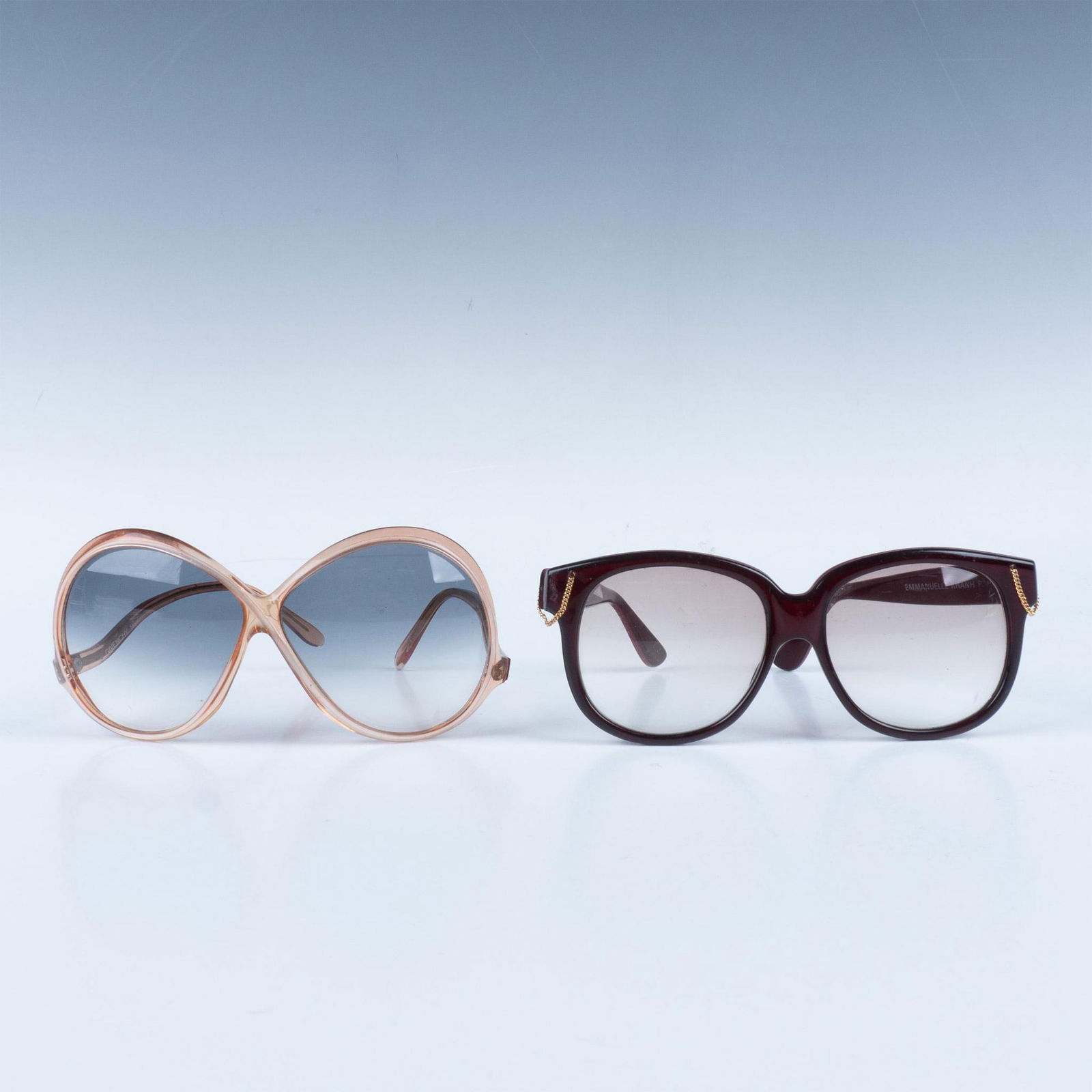 2pc Vintage Designer Sunglasses: Gorgeous pair of retro plastic sunglasses. Includes a Givenchy butterfly style frame, and an Emmanuelle Khan Paris purple frame with little gold chains sunglasses. Branded on the sides of the frames,