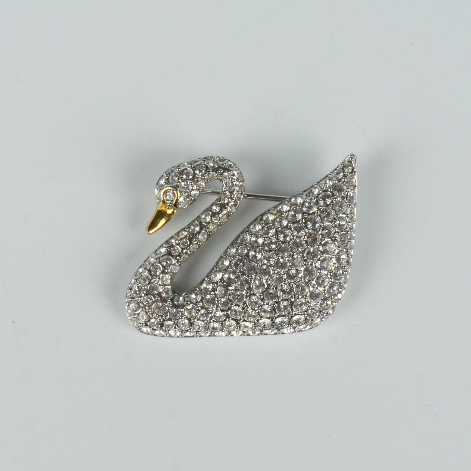 Swarovski Crystal Beautiful Swan Brooch Pin: Silver tone swan with clear crystal-encrusted body and a gold metal face/beak. Swarovski hallmark on the back. Dimensions: 1"L x 1.25"W Manufacturer: Swarovski Country of Origin: Austria