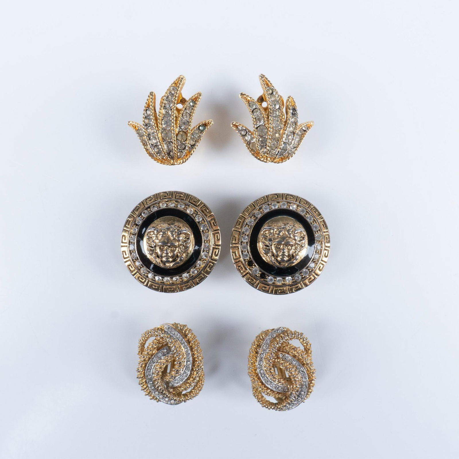 3 Pairs of Vintage Versace Style Gold Clip On Earrings: Gorgeous group of gold toned with incrusted rhinestones and black enameling, featuring the stylish Versace design and the iconic Medusa head buttons. Marked, Gio and Kenneth Lane. Largest pair dimensi