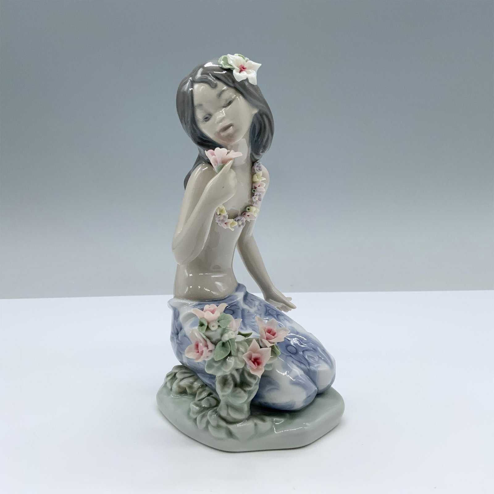 In a Tropical Garden 1001479 - Lladro Porcelain Figurine: Glossy finish. Features a charming girl smelling a flower. Lladro backstamp. This item has its original box. Box measures 8"L x 5"W x 4.75"H. Artist: Salvador Debon Issued: 1985 - 1995 Dimensions: 3.7
