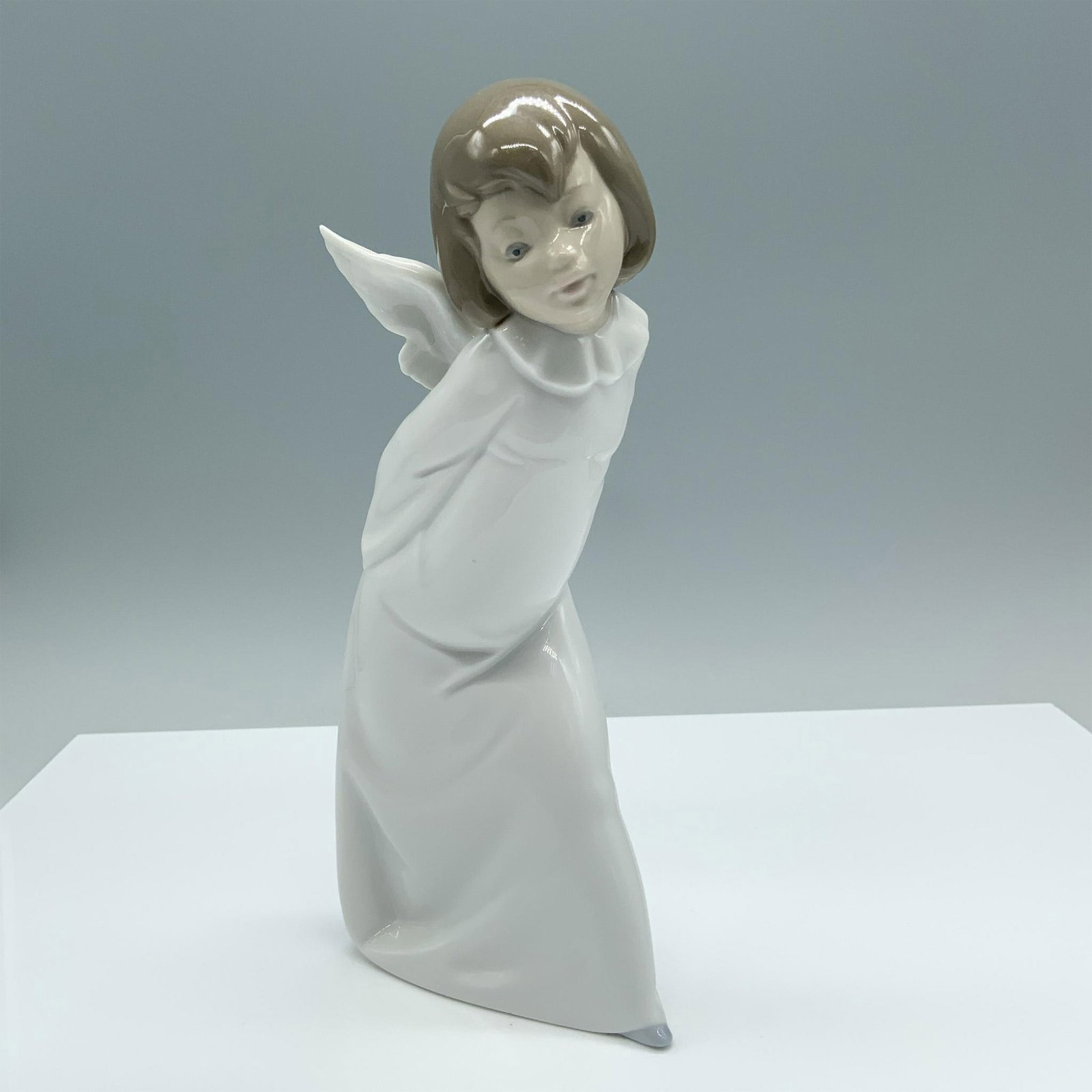 Curious Angel 01004960 - Lladro Porcelain Figurine: Glossy finish. Features a charming angel dressed in a white robe holding a candle. Lladro backstamp. Artist: Salvador Debon Issued: 1977 Dimensions: 4.5"L x 3.5"W x 9.25"H Manufacturer: Lladro Countr