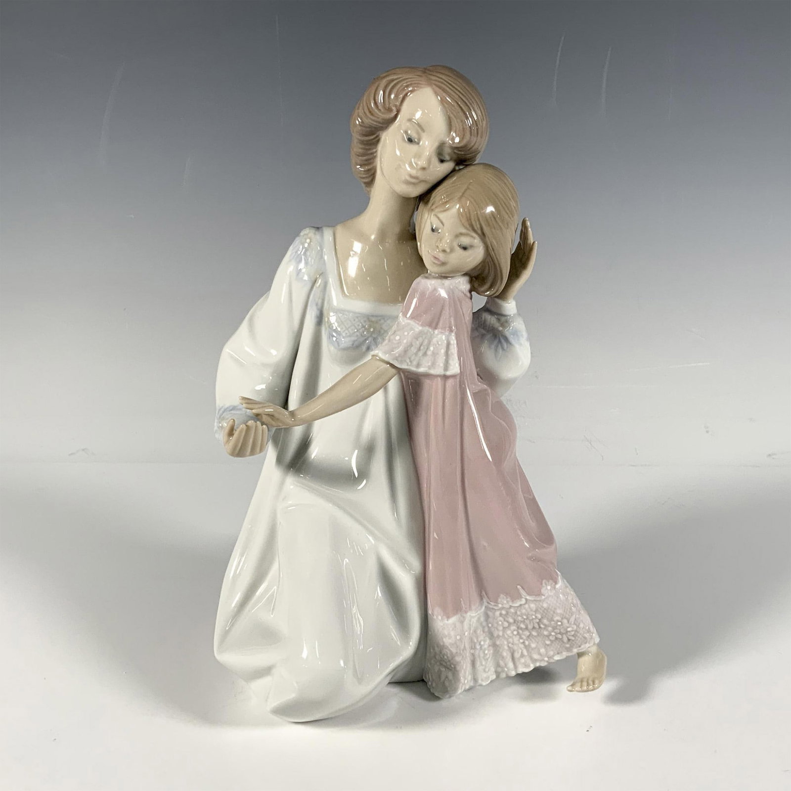 Good Night - Lladro Porcelain Figurine: Beautiful glazed porcelain depiction of a mother and daughter in their night dresses. Both have short, light brown hair. Mother is in white with blue accents and the daughter is in pink and white. Ite