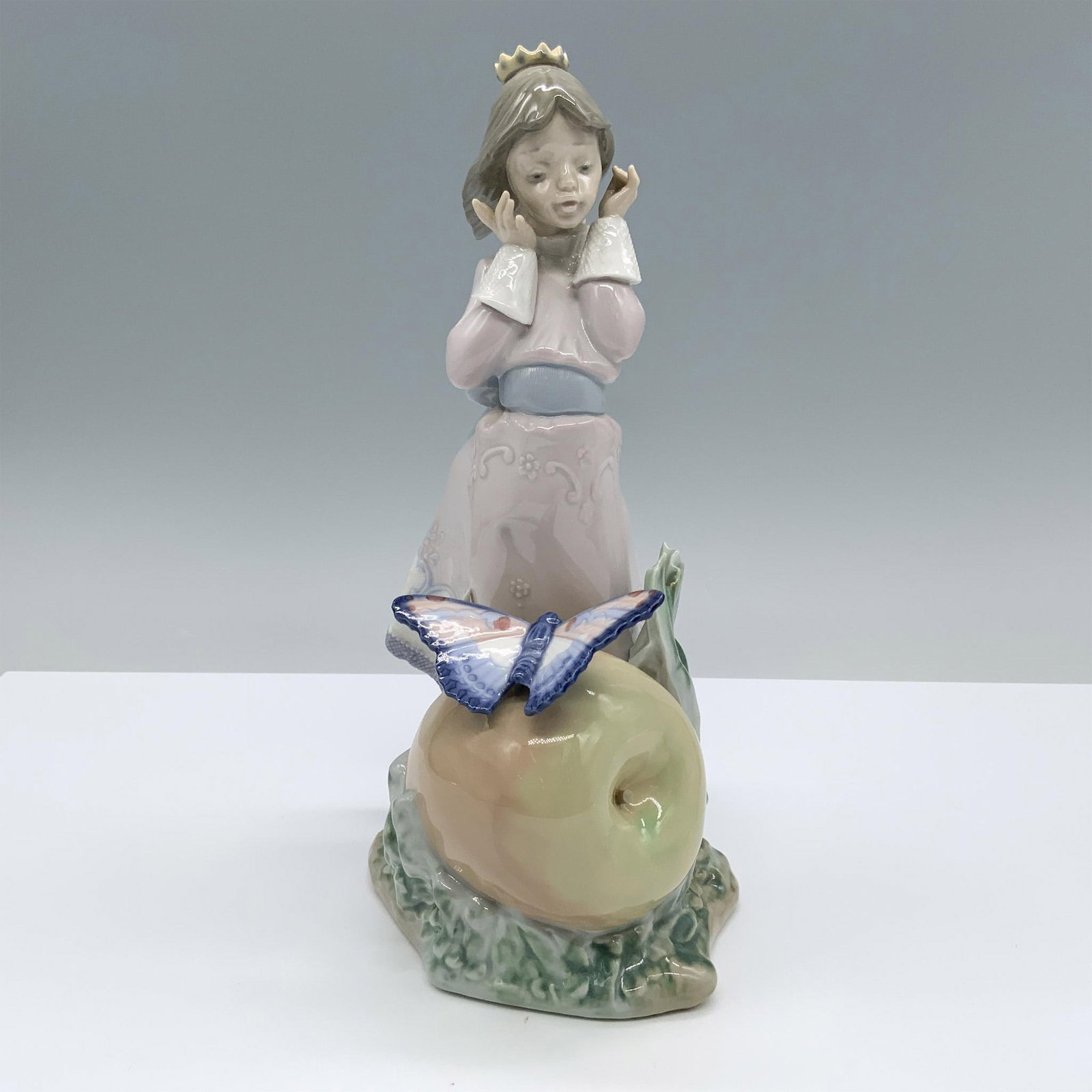 Land of the Giants 1005716 - Lladro Porcelain Figurine: Glossy finish. Features a charming girl in a gown, being swept by the breeze with a giant peach and a butterfly. Lladro backstamp. This item has its original box. Box measures 7.5"L x 12.5"W x 6"H. Ar